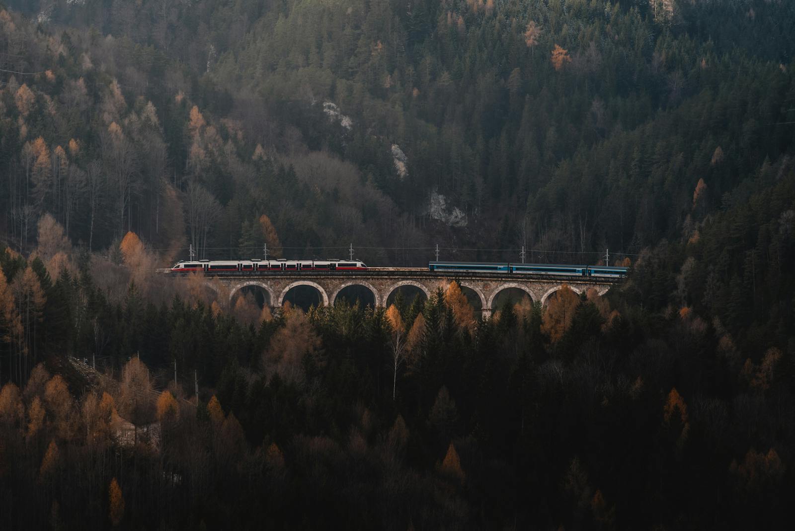 A scenic train travels across the historic Semmering Viaduct amidst the autumn forest in Austria.