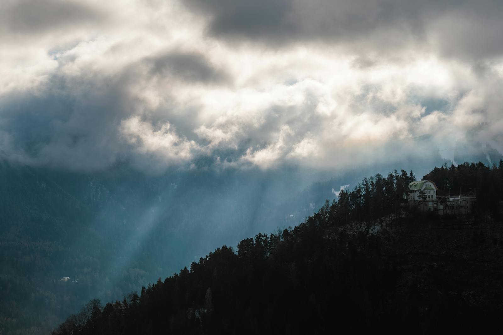 Captivating view of sunlight piercing through clouds over Austrian mountains.