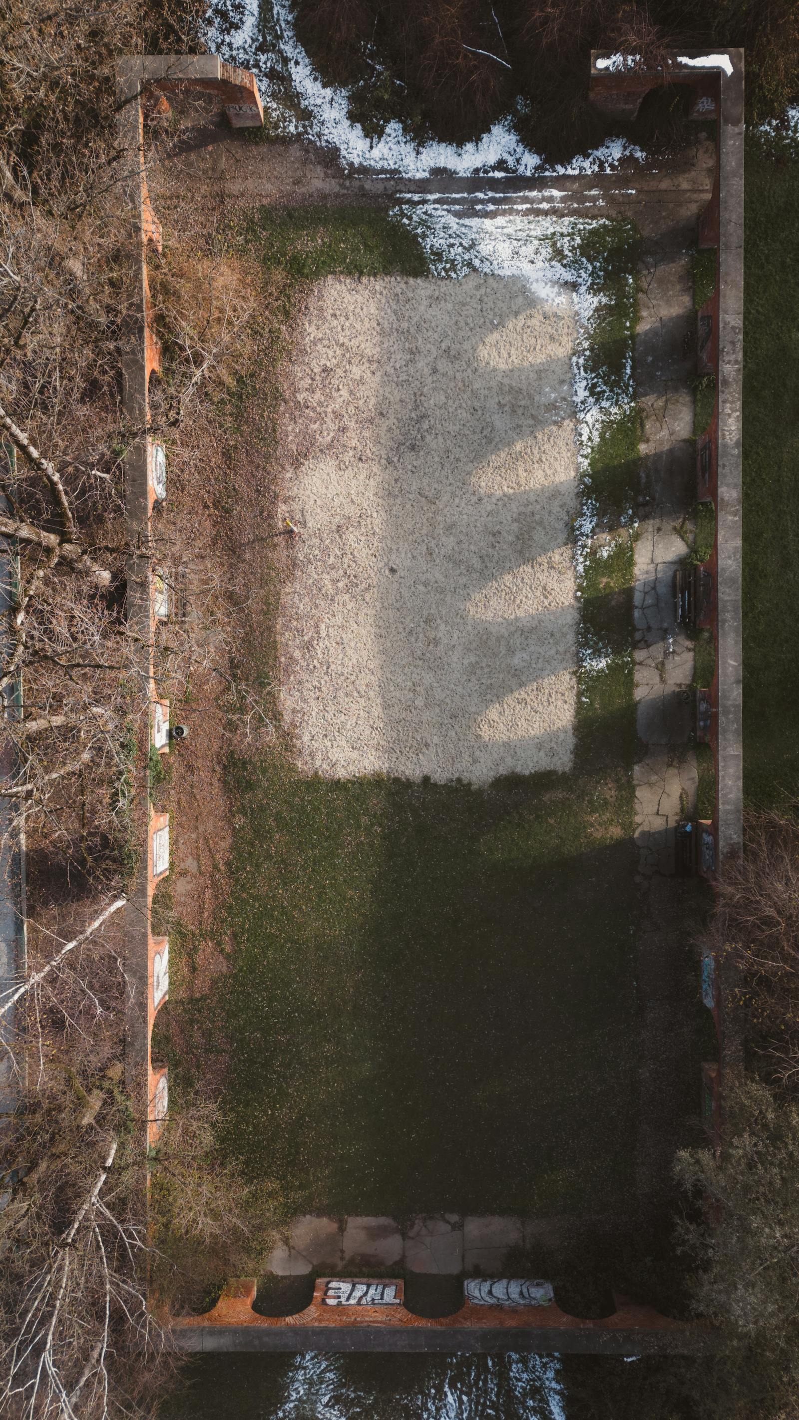 Drone shot of an overgrown field surrounded by brick walls in Graz, Austria, showing nature reclaiming space.