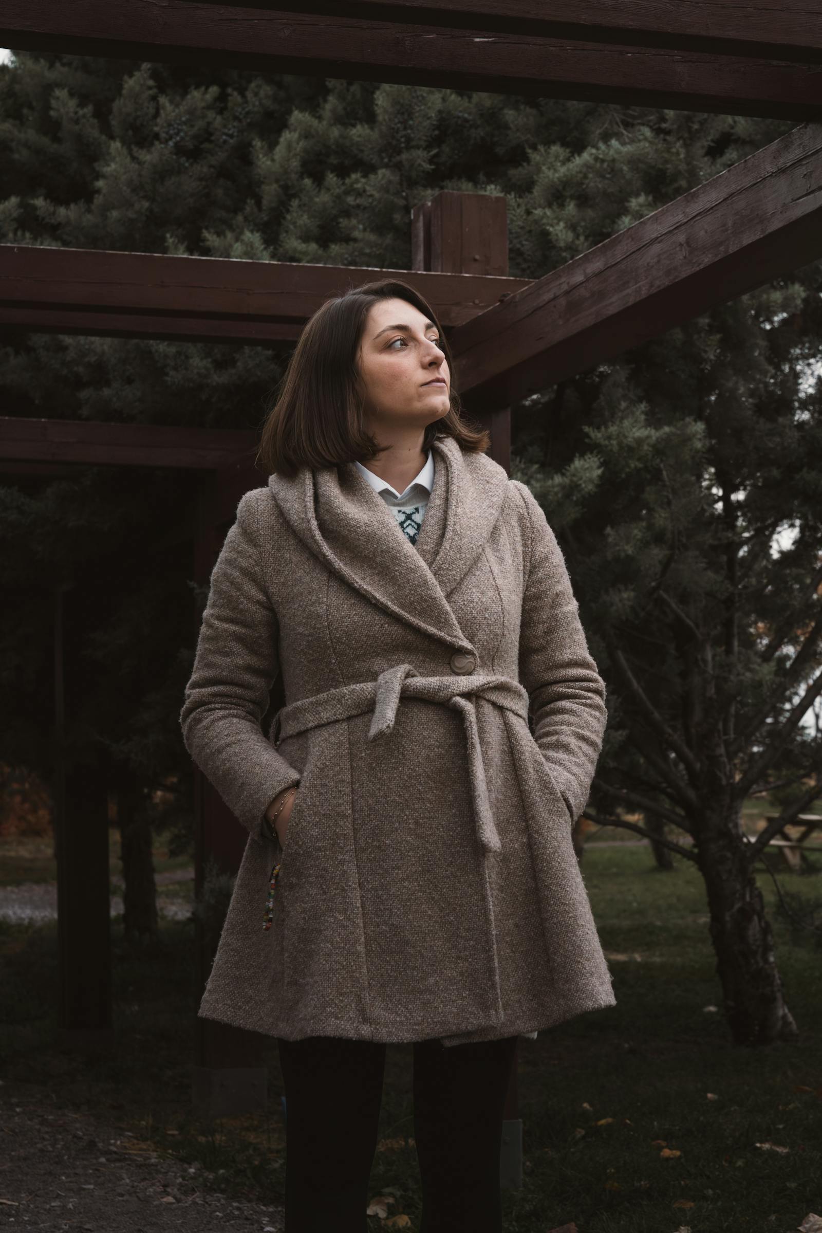 Woman in a stylish coat reflects under pergola in Ankara autumn park.