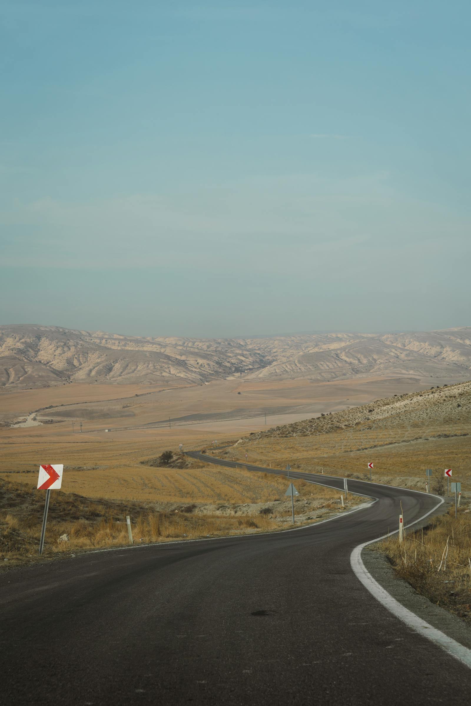 A winding road traverses the vast, rolling hills of Ankara's countryside, showcasing Turkey's striking natural beauty.