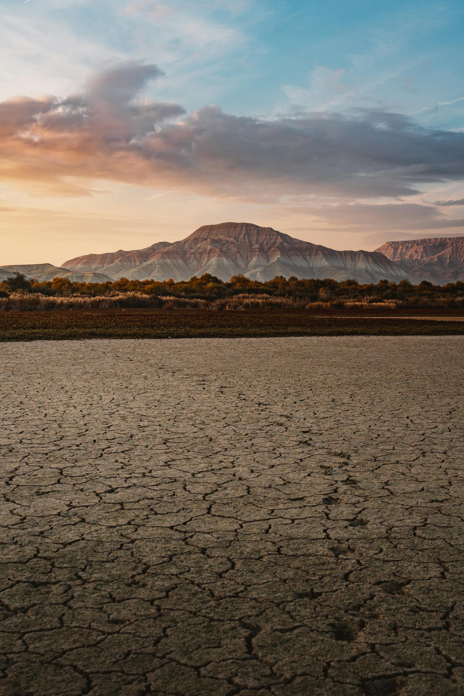 Beautiful view of arid cracked earth in front of a mountain range at sunset, showcasing nature's raw beauty.