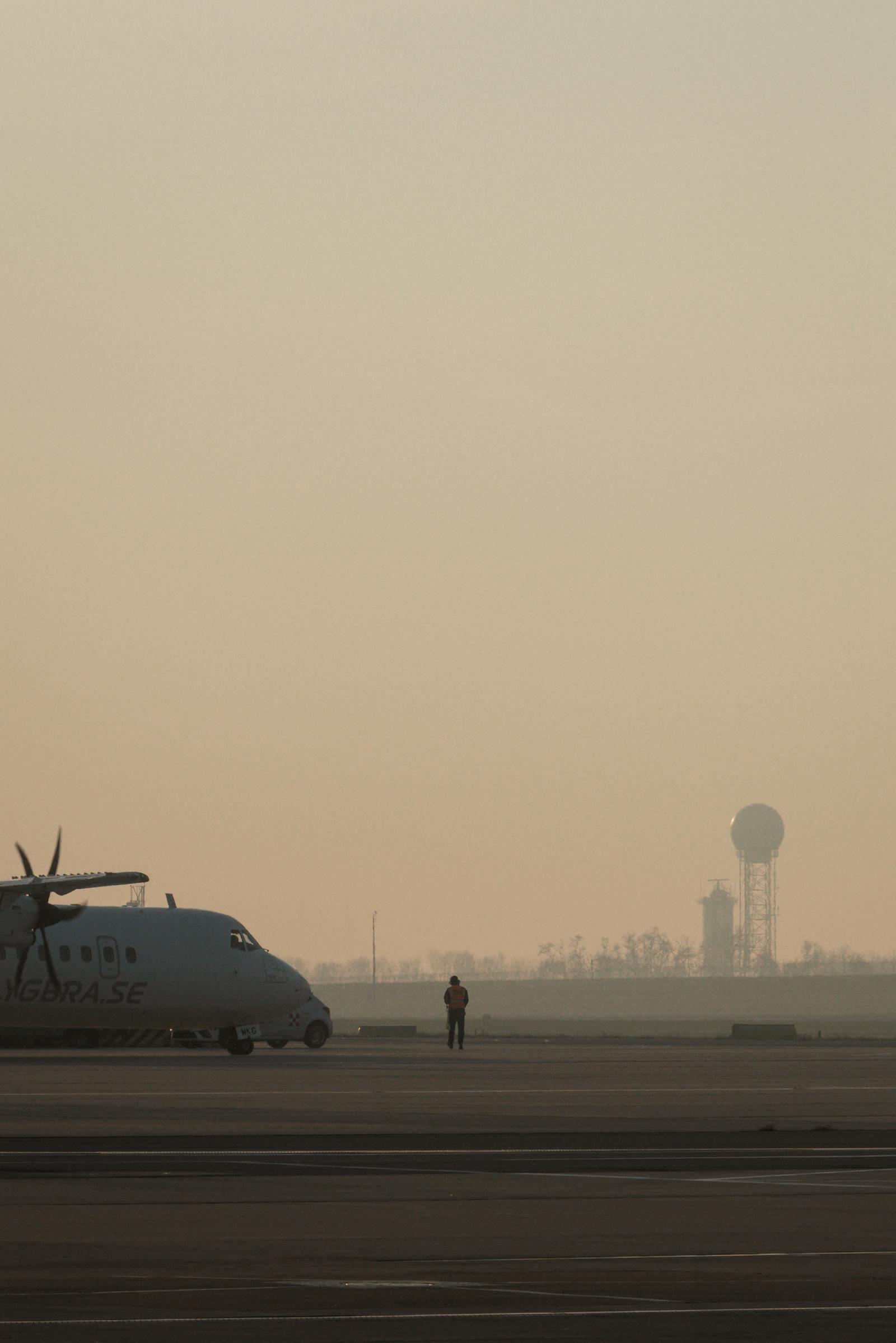 An early morning scene at Schwechat Airport, featuring a solitary figure and aircraft against a hazy sky.