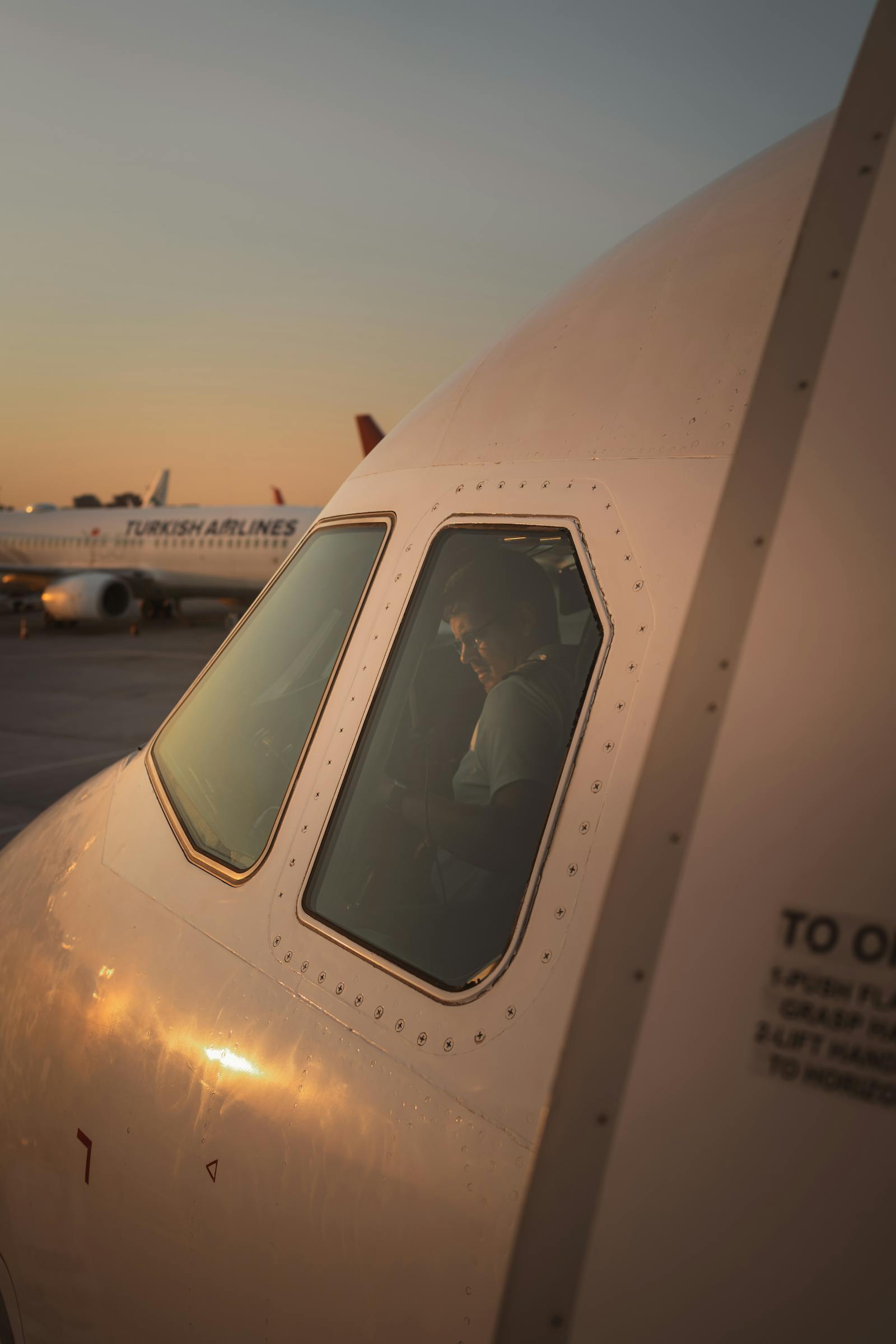 Close-up of airplane cockpit window with pilot at sunset, creating a warm aviation scene.