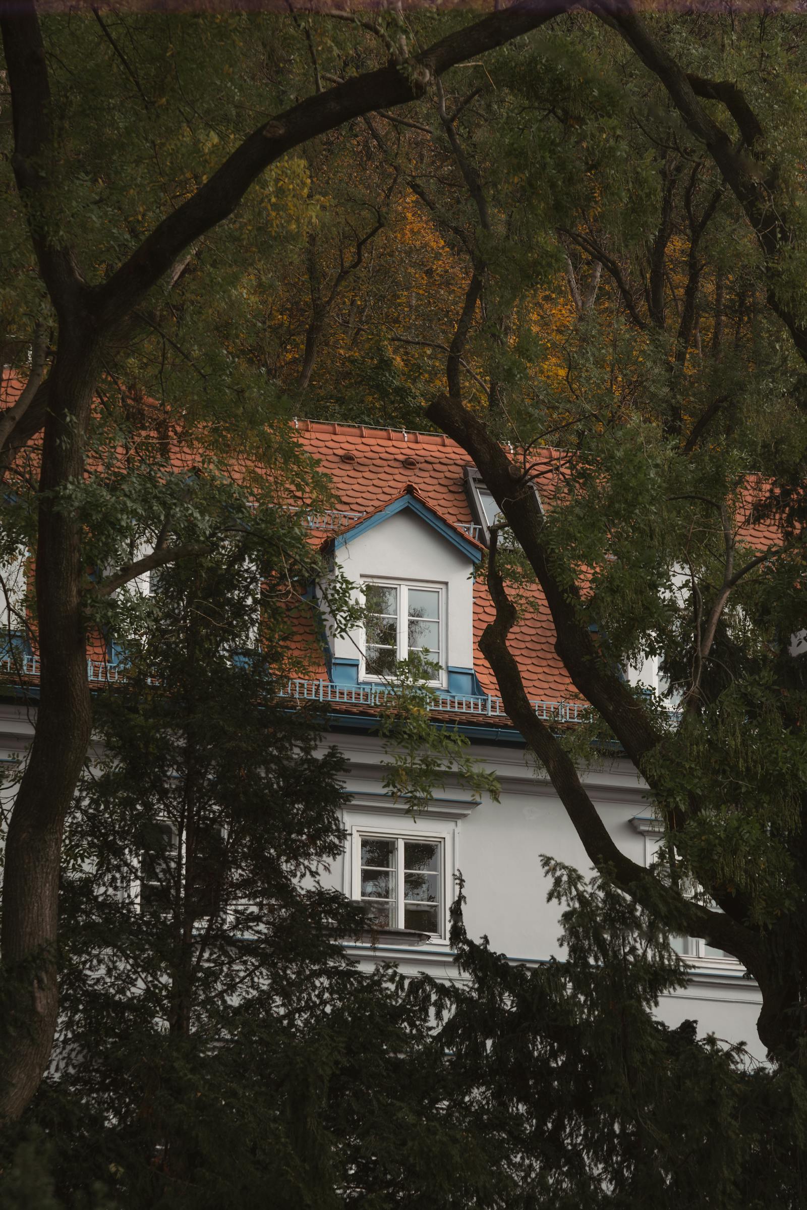 Serene cottage with red roof surrounded by lush trees in fall season, offering a tranquil retreat.