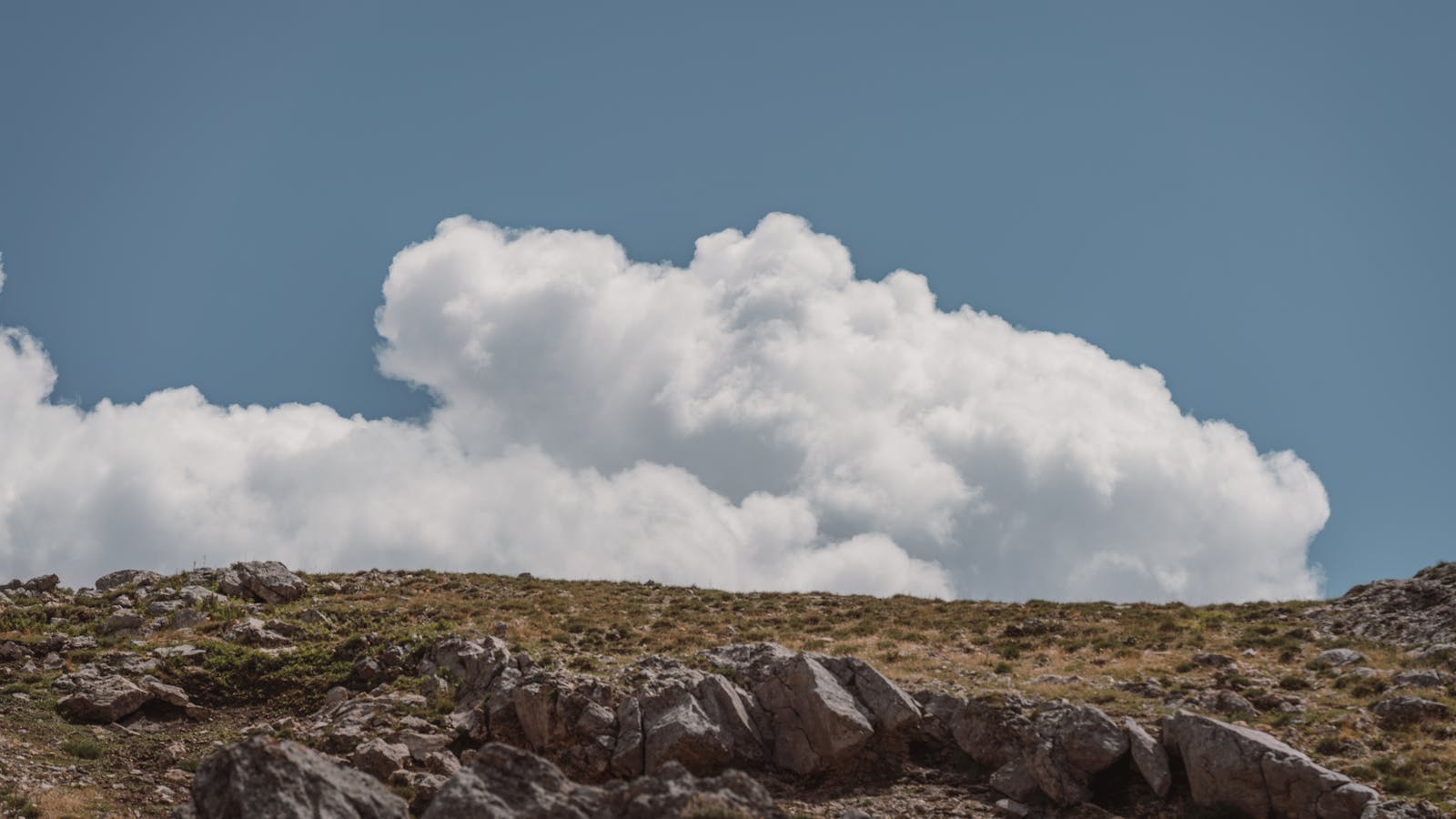 A tranquil scene capturing fluffy clouds over a rocky hill in Seydişehir, Turkey.