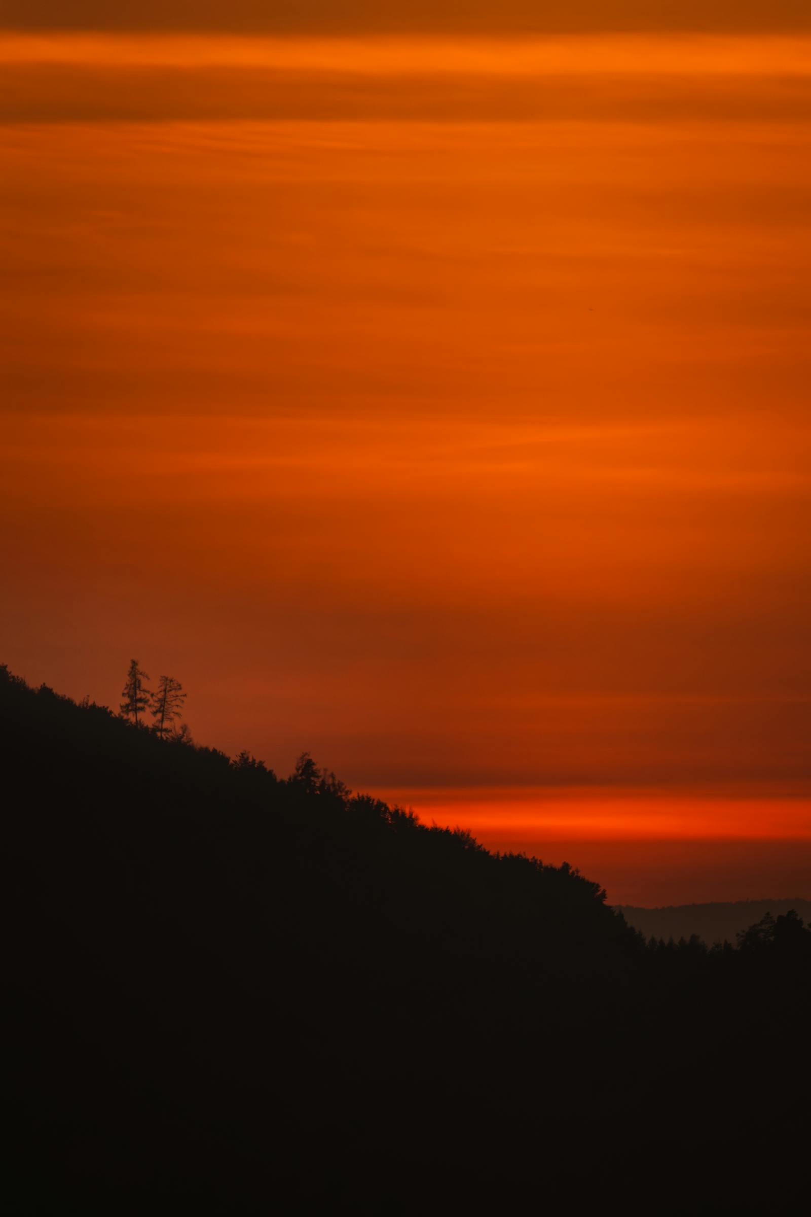 Beautiful orange sunset casting silhouettes over the hills of Graz, Austria. Tranquil landscape with serene evening light.