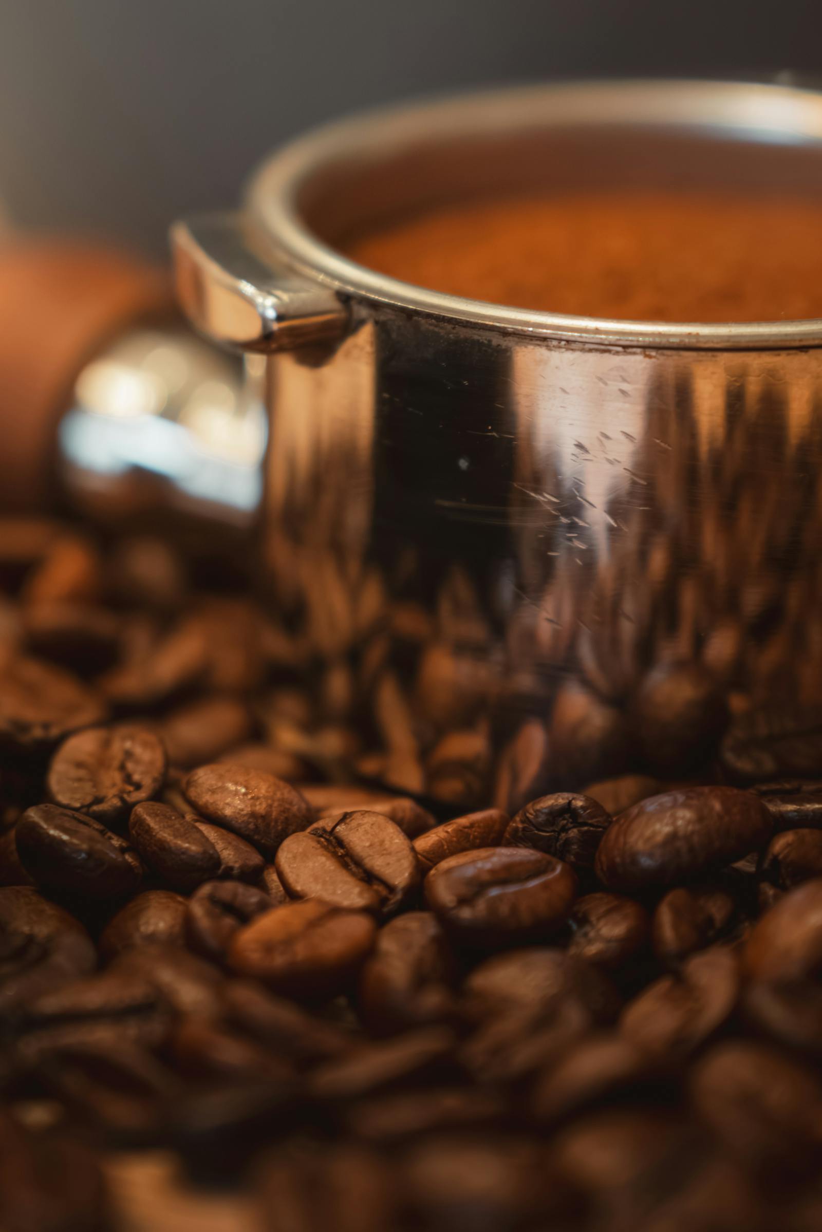 Rich coffee beans surrounding a stainless steel espresso pot, creating a warm and inviting scene.