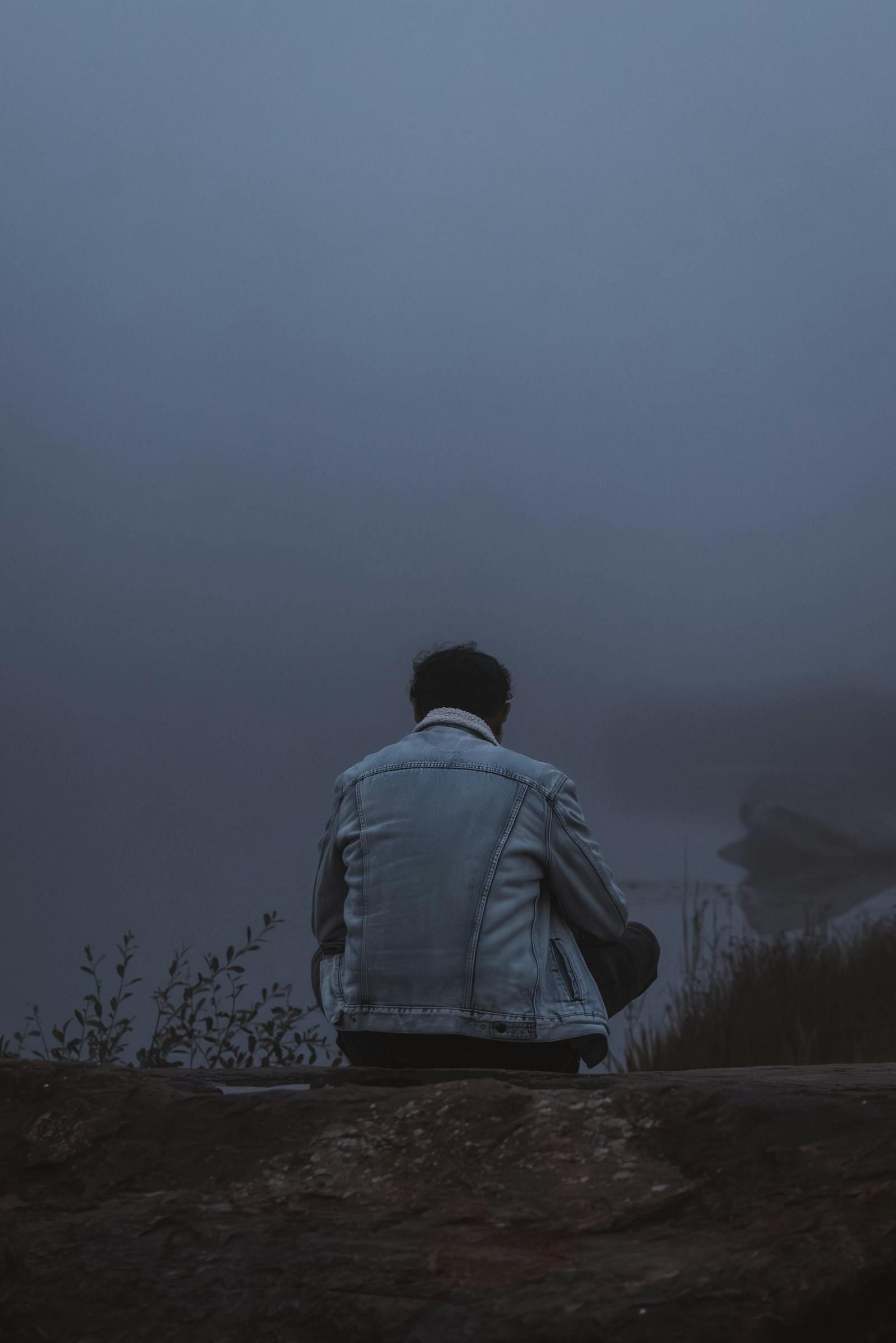 A person in a denim jacket sits alone in a misty, tranquil setting in Styria, Austria.