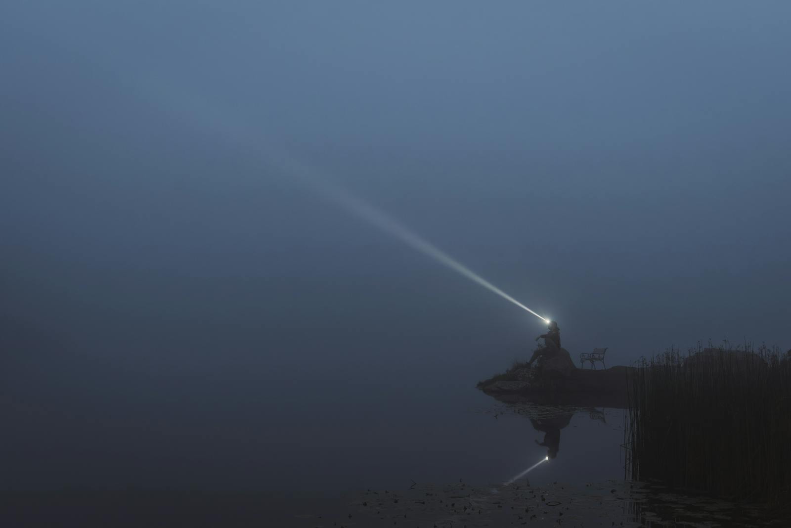 Mystical spotlight beams through foggy night on an isolated island in Styria, Austria.