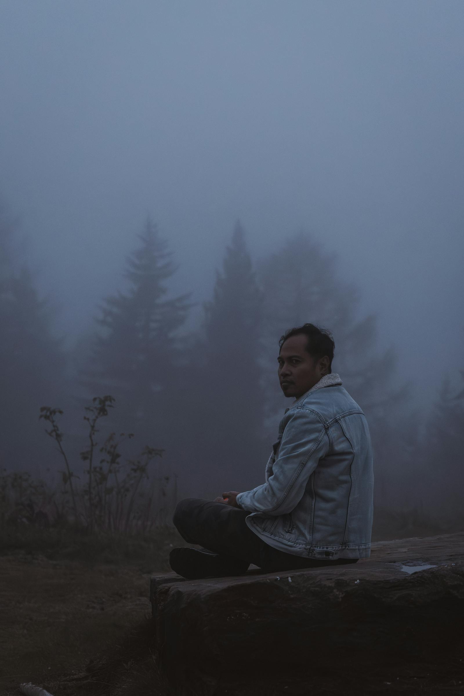 A contemplative man sits quietly in the misty woods of Styria, Austria, evoking a serene and introspective mood.