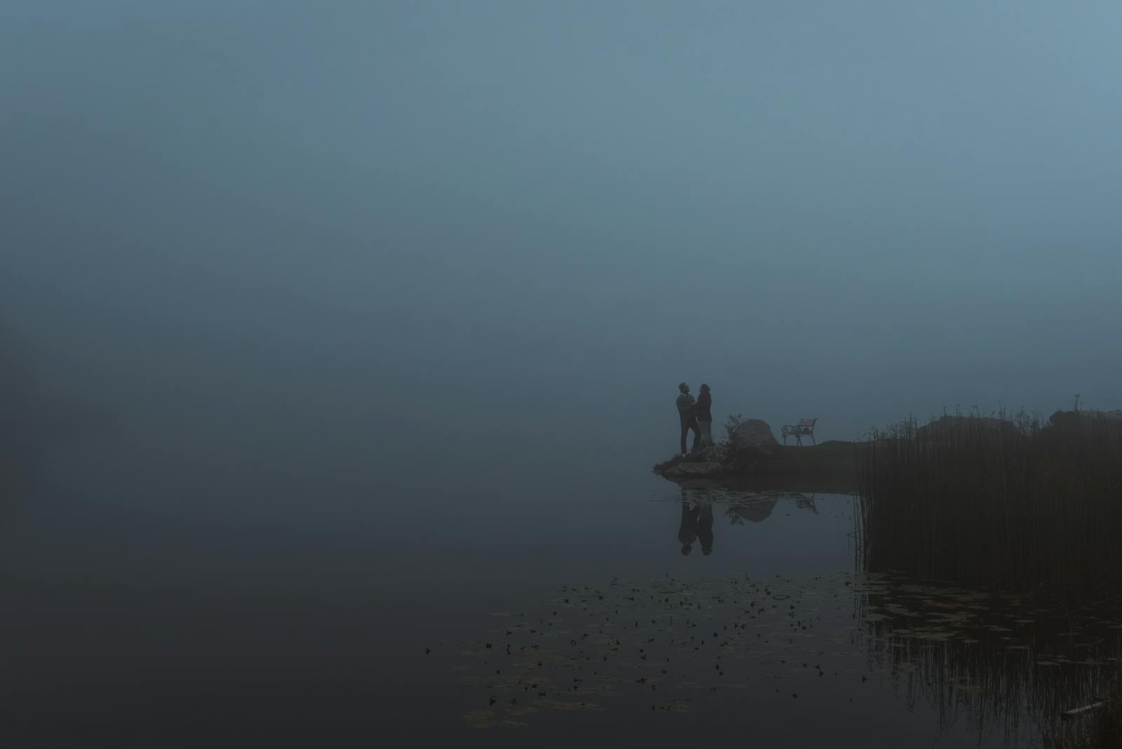 Silhouetted figures on a foggy lakeside in Styria, Austria, exuding tranquility.