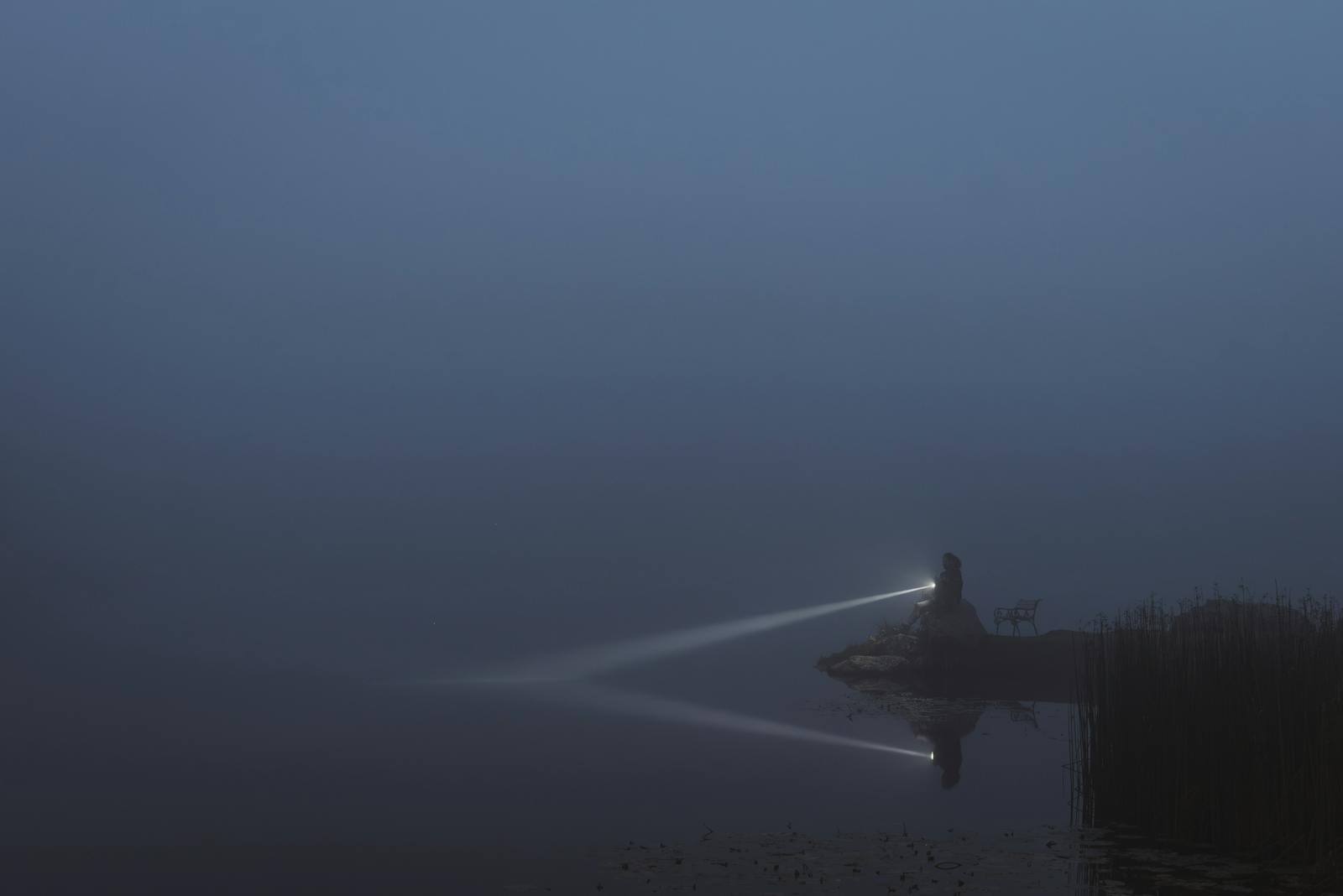 Serene lakeside scene with flashlight reflection illuminating misty night in Austria.