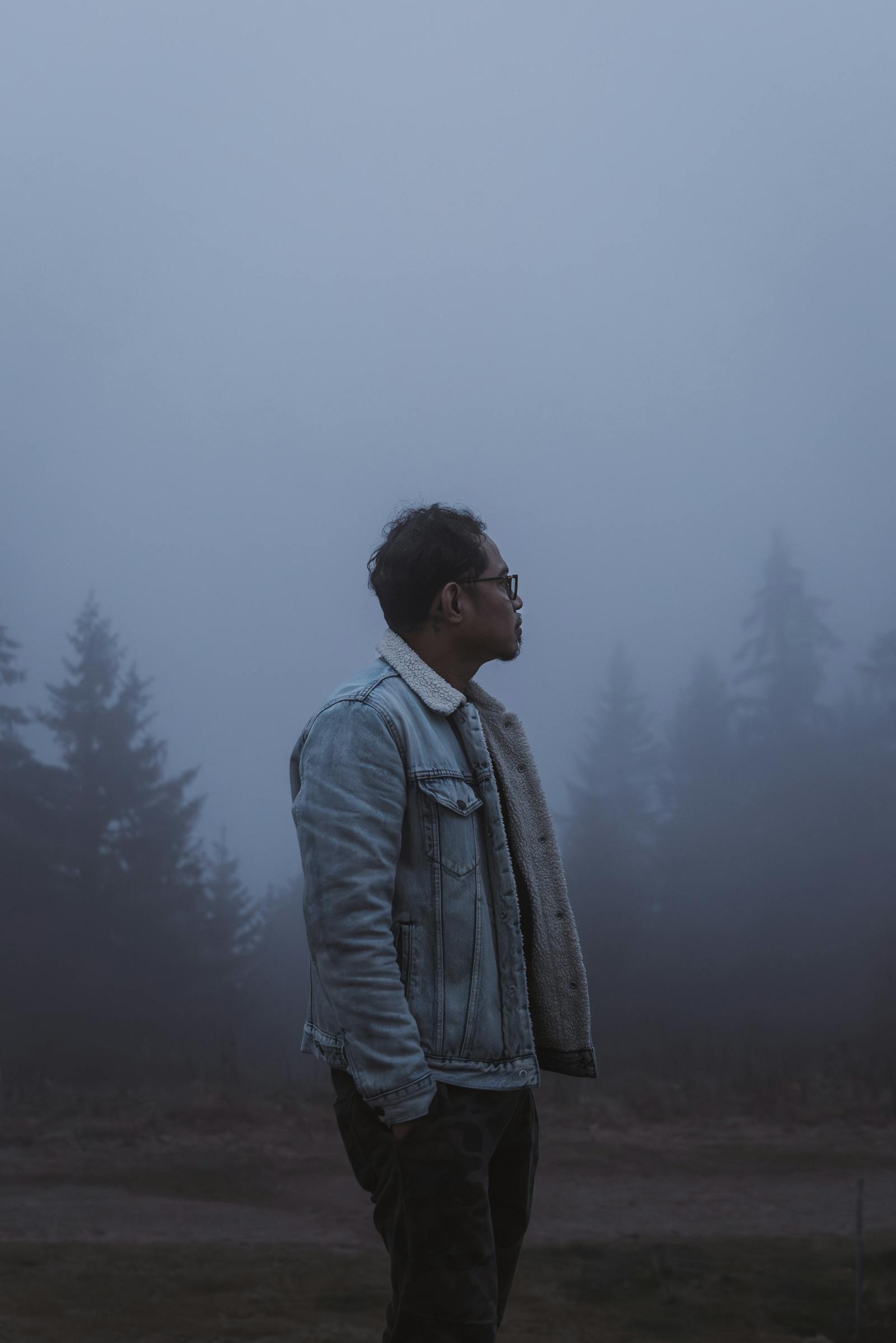 A man in a denim jacket stands contemplatively in a misty forest in Styria, Austria.