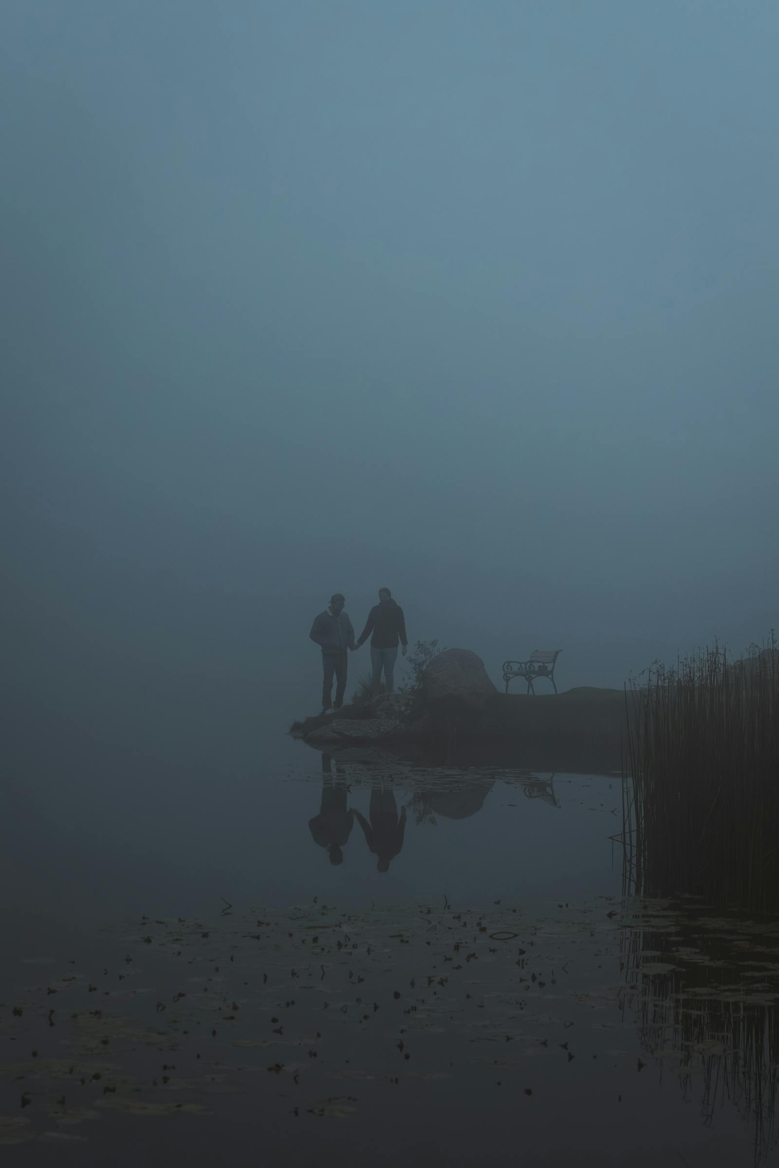 Couple holding hands on a misty lake shore in Styria, Austria, evoking tranquility and solitude.