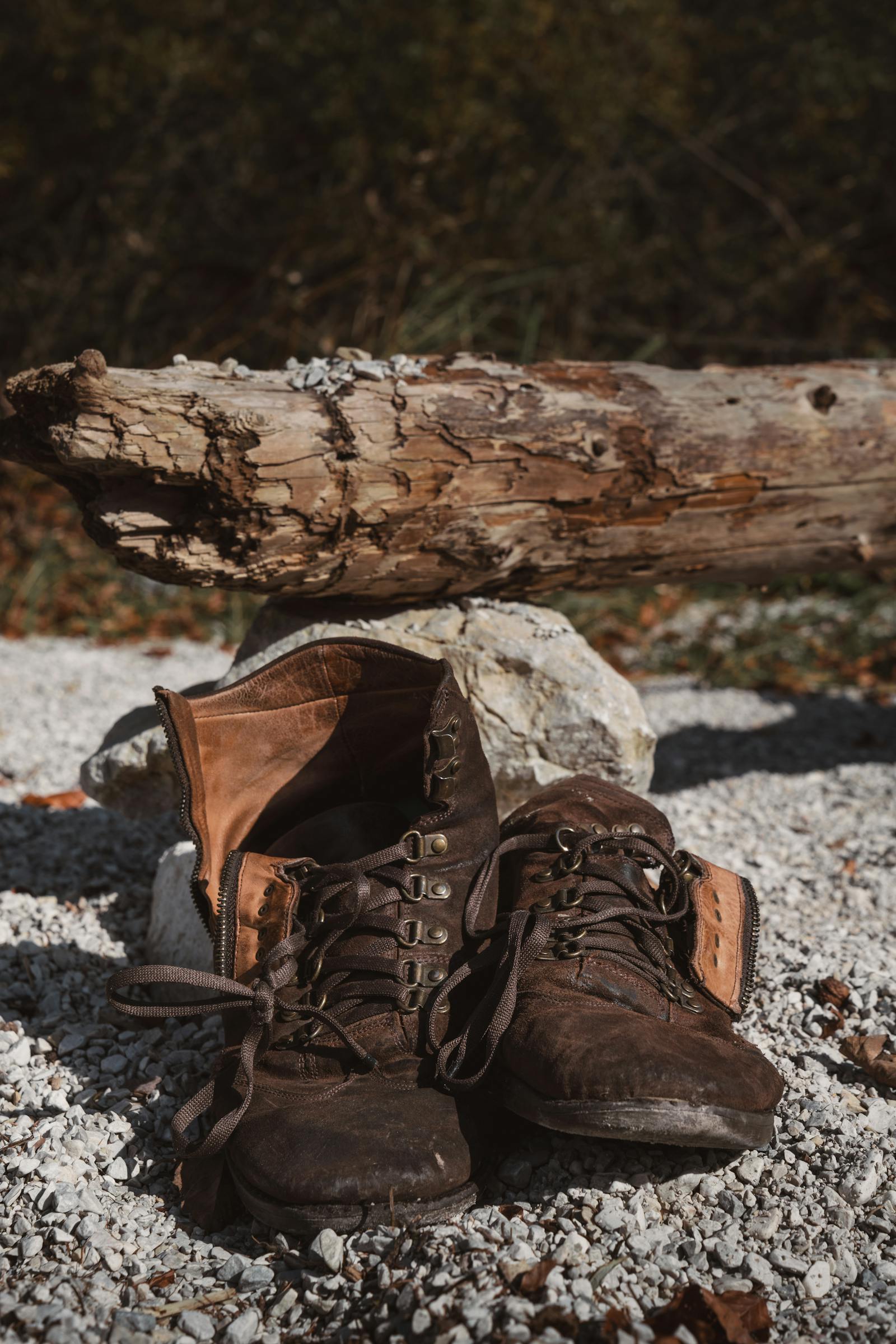 Rugged vintage hiking boots resting on a gravel path with rustic log backdrop.