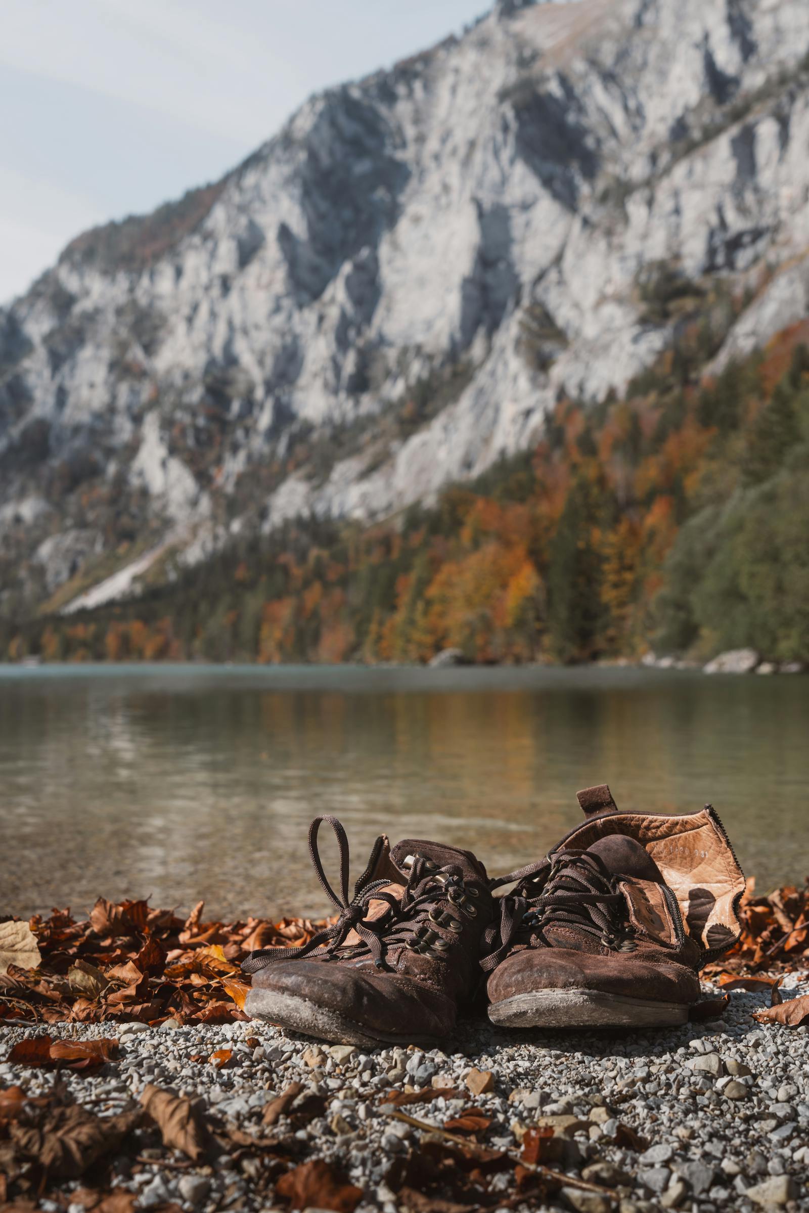 Hiking shoes by a tranquil alpine lake with autumn foliage and mountains in the background.