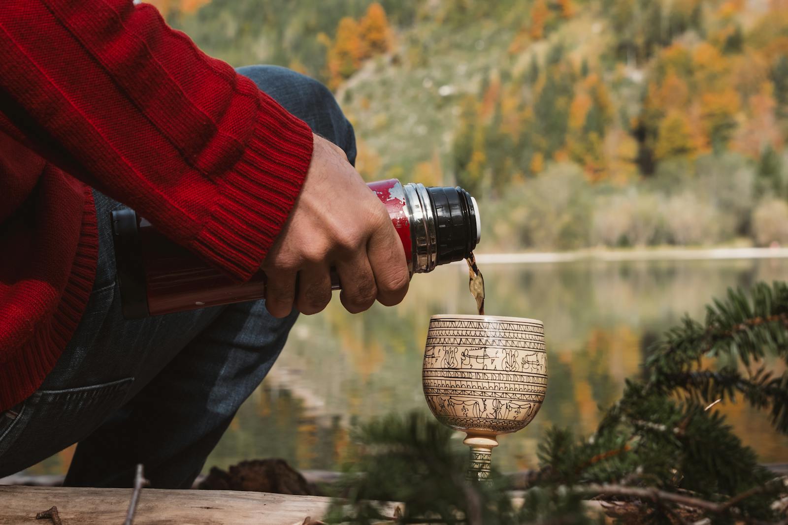 A serene autumn scene in Styria, Austria, with a cozy moment by the lake, featuring hand pouring hot drink.