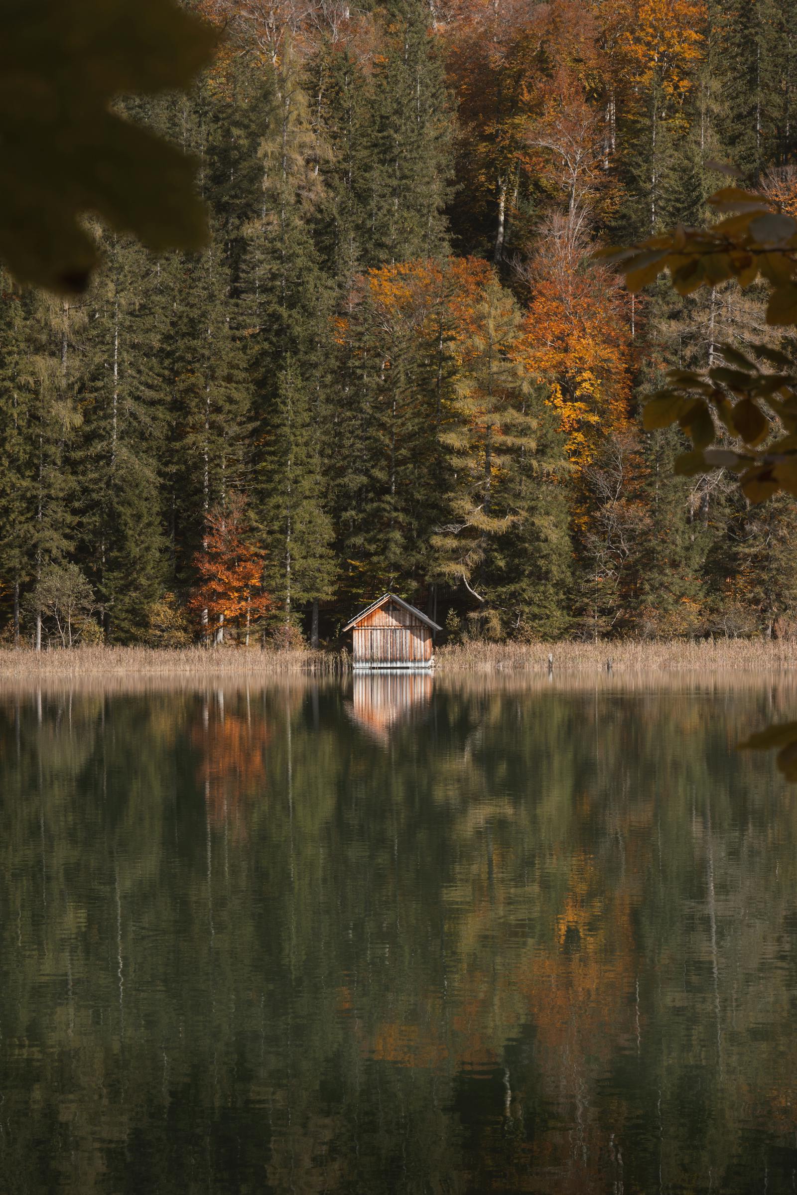 Serene autumn scenery with a cabin reflecting on a calm mountain lake in Eisenerz, Austria