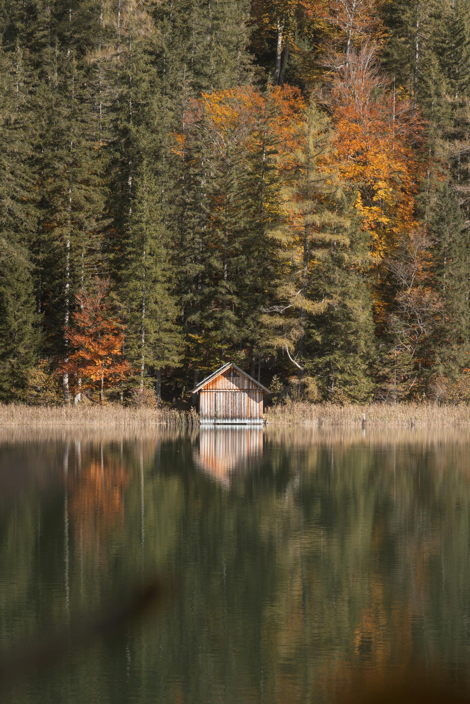 Serene autumn scenery with a cabin reflecting in a tranquil lake surrounded by colorful trees in Eisenerz, Austria.