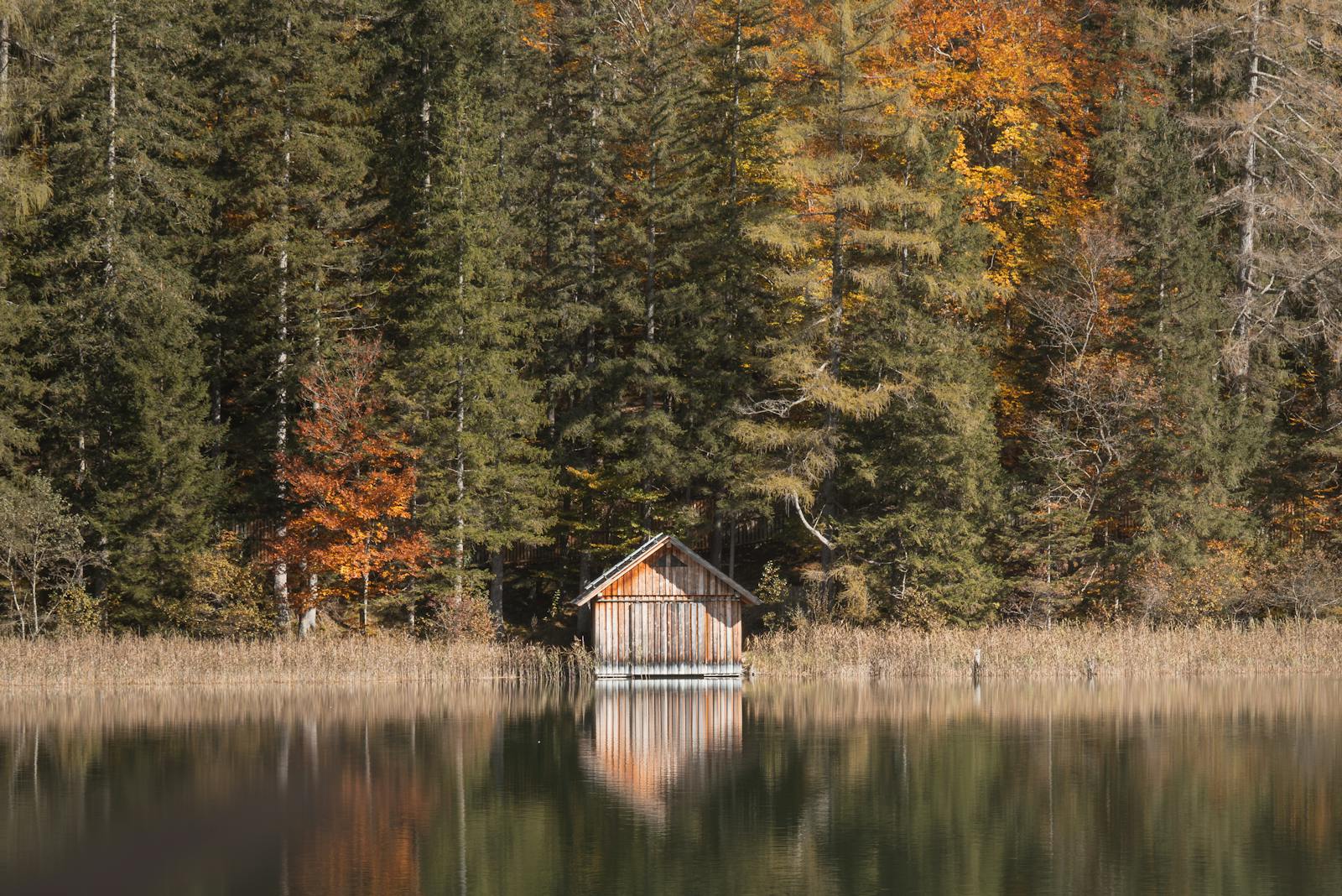 A serene cabin by a forested lake in autumn, reflecting calm and nature's beauty.