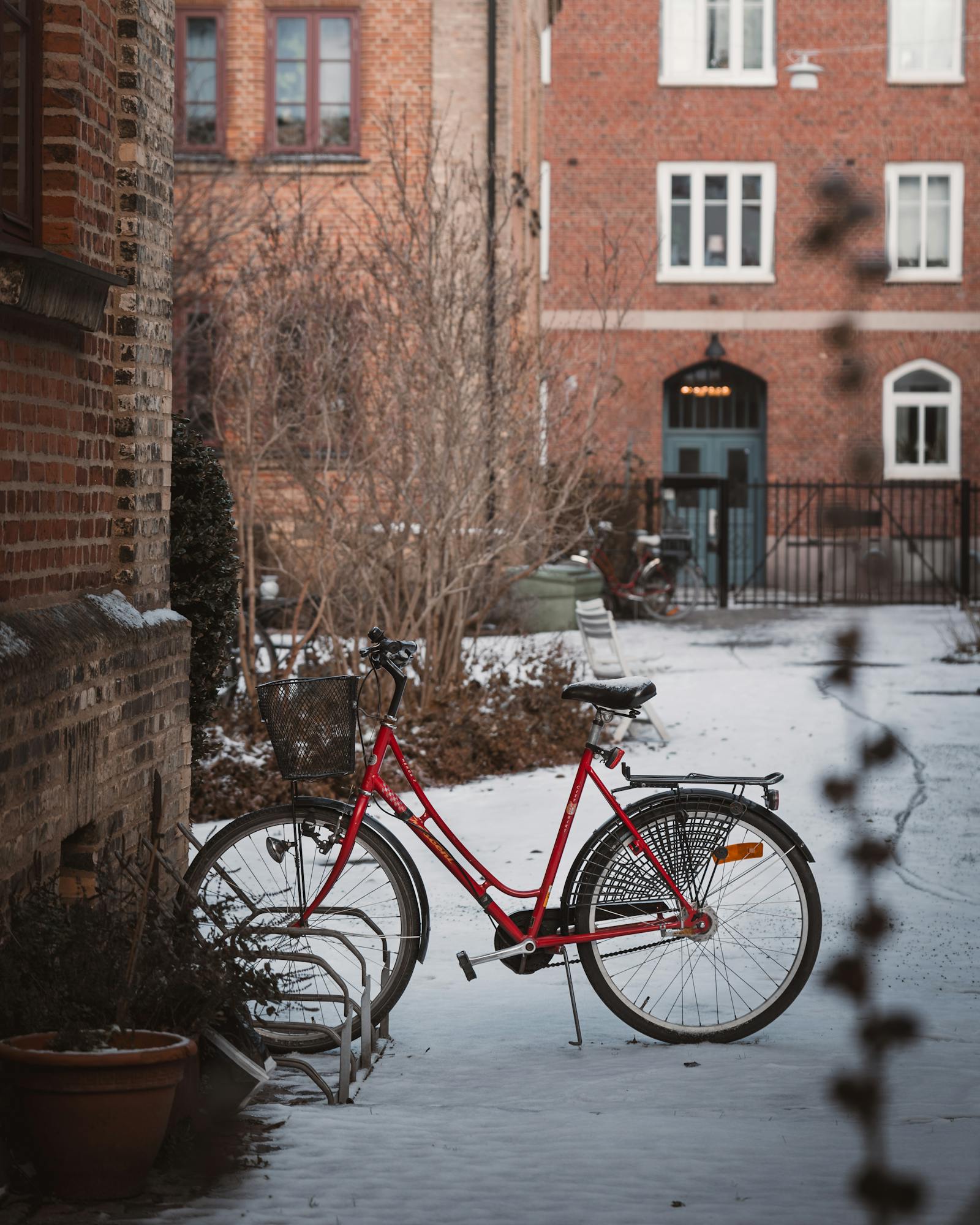 A serene, snow-dusted courtyard featuring a parked red bicycle against a brick wall.