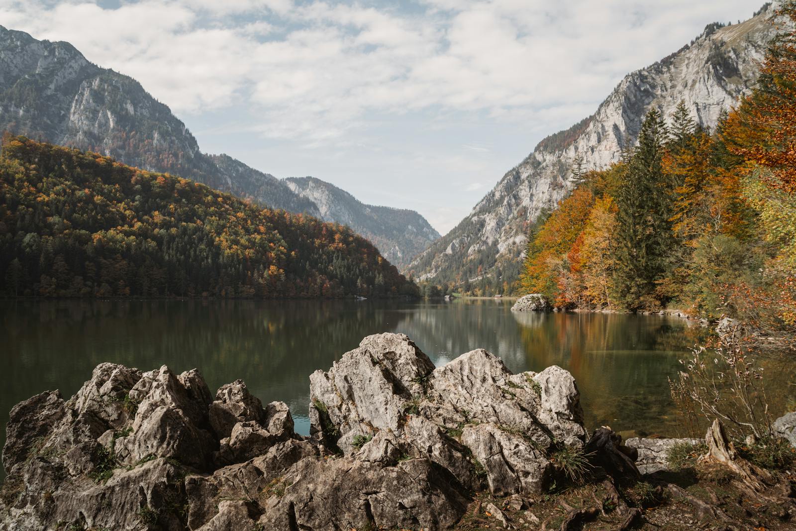 Tranquil Austrian lake surrounded by rugged mountains and vibrant autumn foliage.