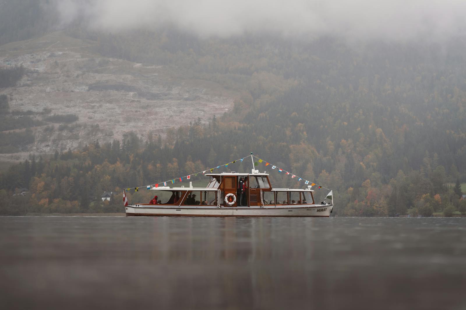 Serene autumn landscape featuring a boat on a misty lake amid tranquil mountainous surroundings.