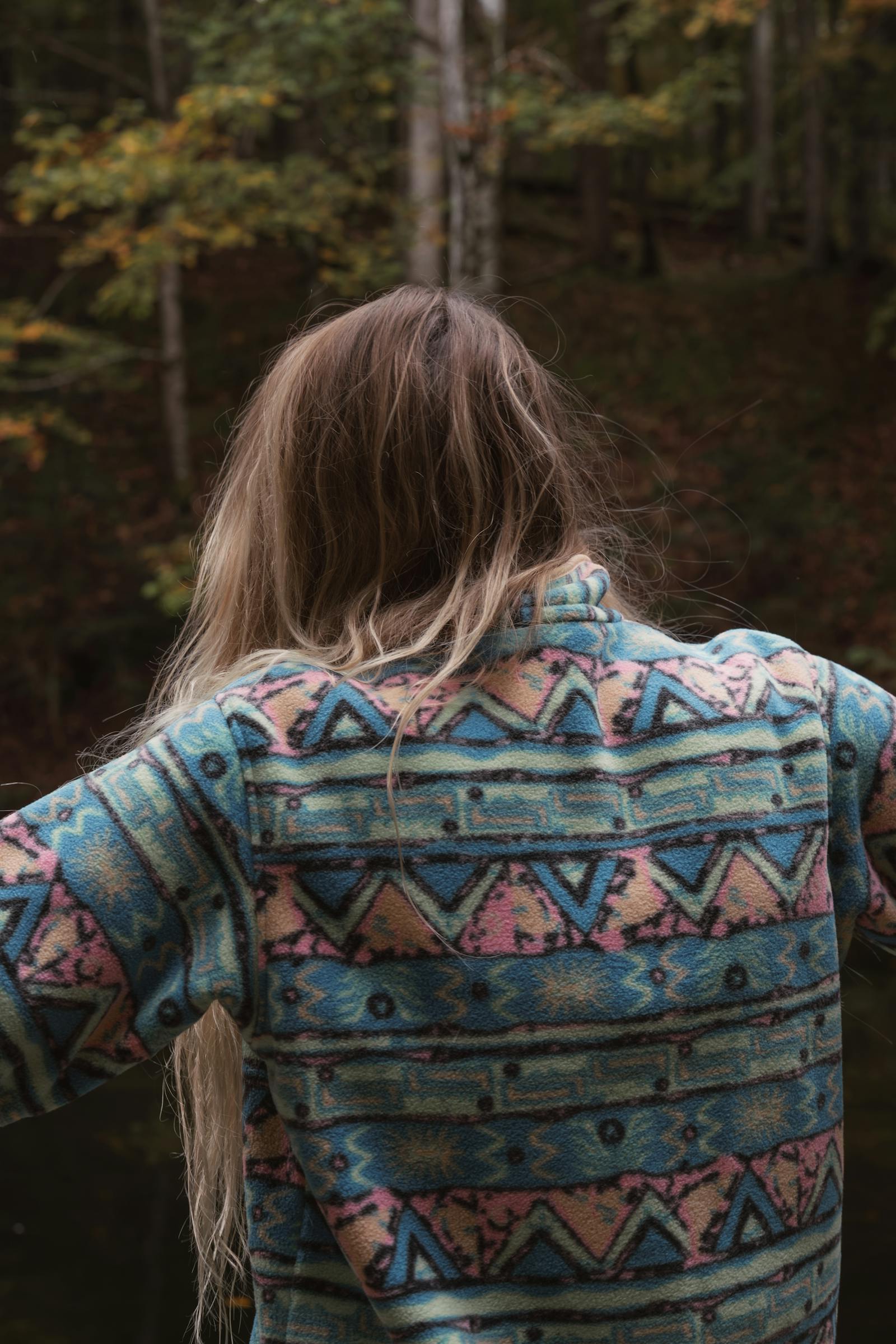 Woman in patterned sweater enjoying peaceful moment in the woods during fall.