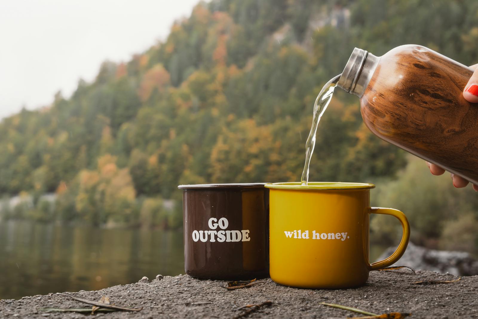 Pouring coffee into mugs by a serene lake in Austria, surrounded by autumn foliage.