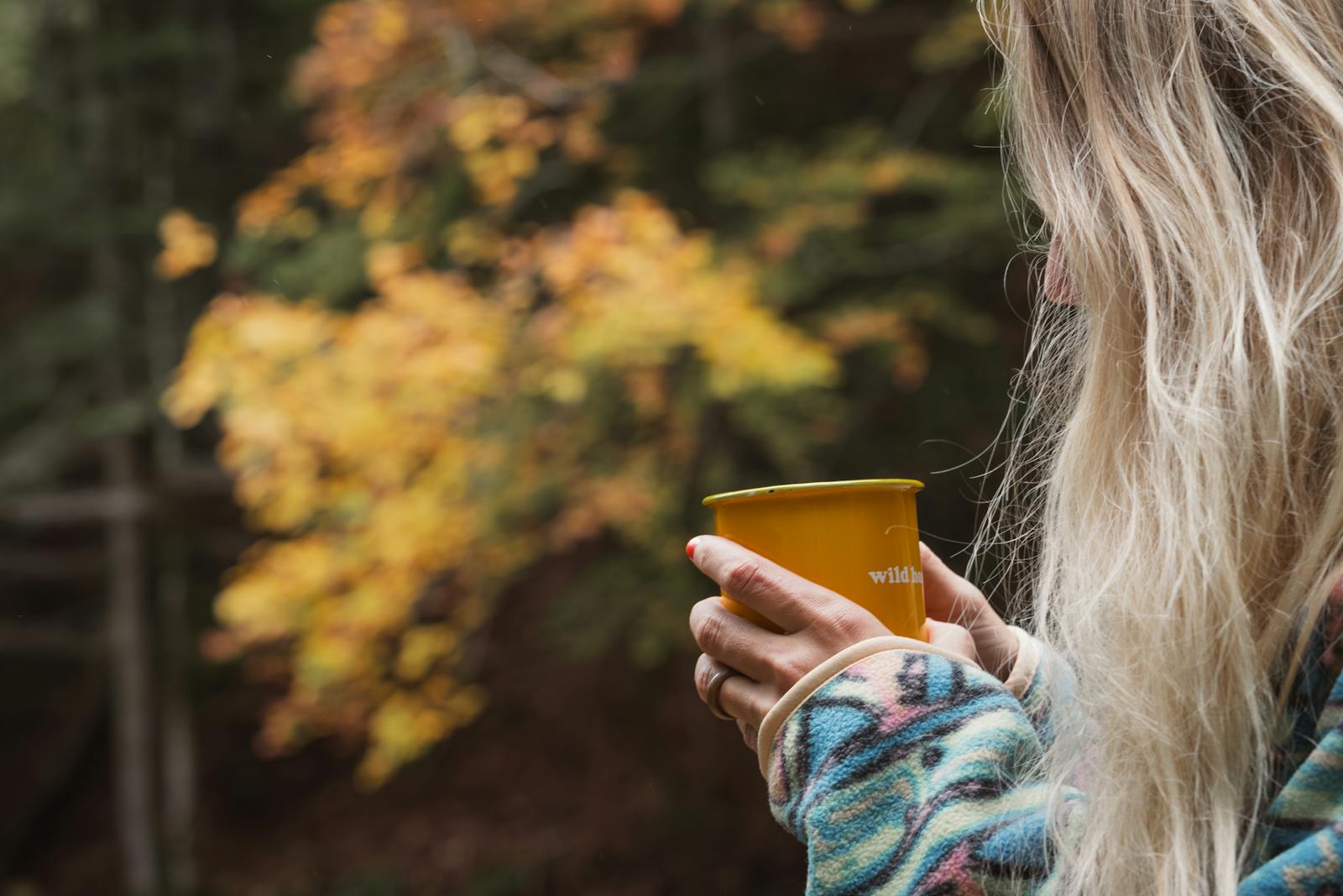 Woman enjoying a mindful moment with a warm drink in the autumn woods of Styria, Austria.