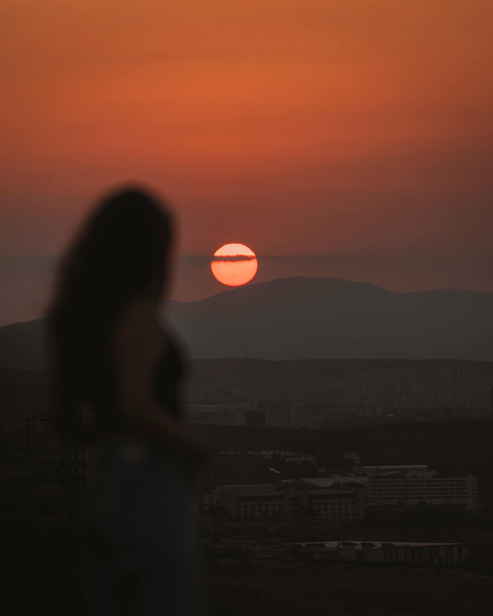 Silhouette of a woman with the sun setting over the hills of Ankara, Türkiye.