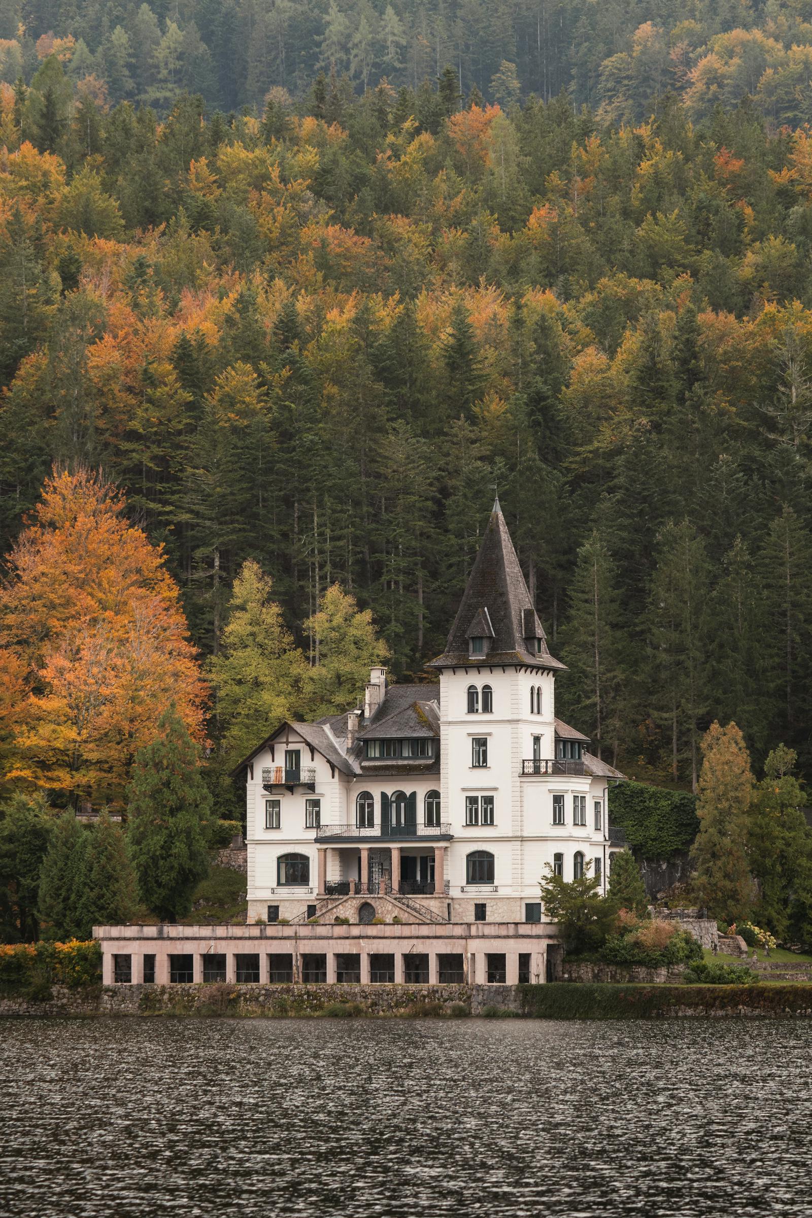 A picturesque castle by a serene lake with a vibrant autumn forest backdrop in Bad Aussee, Austria.