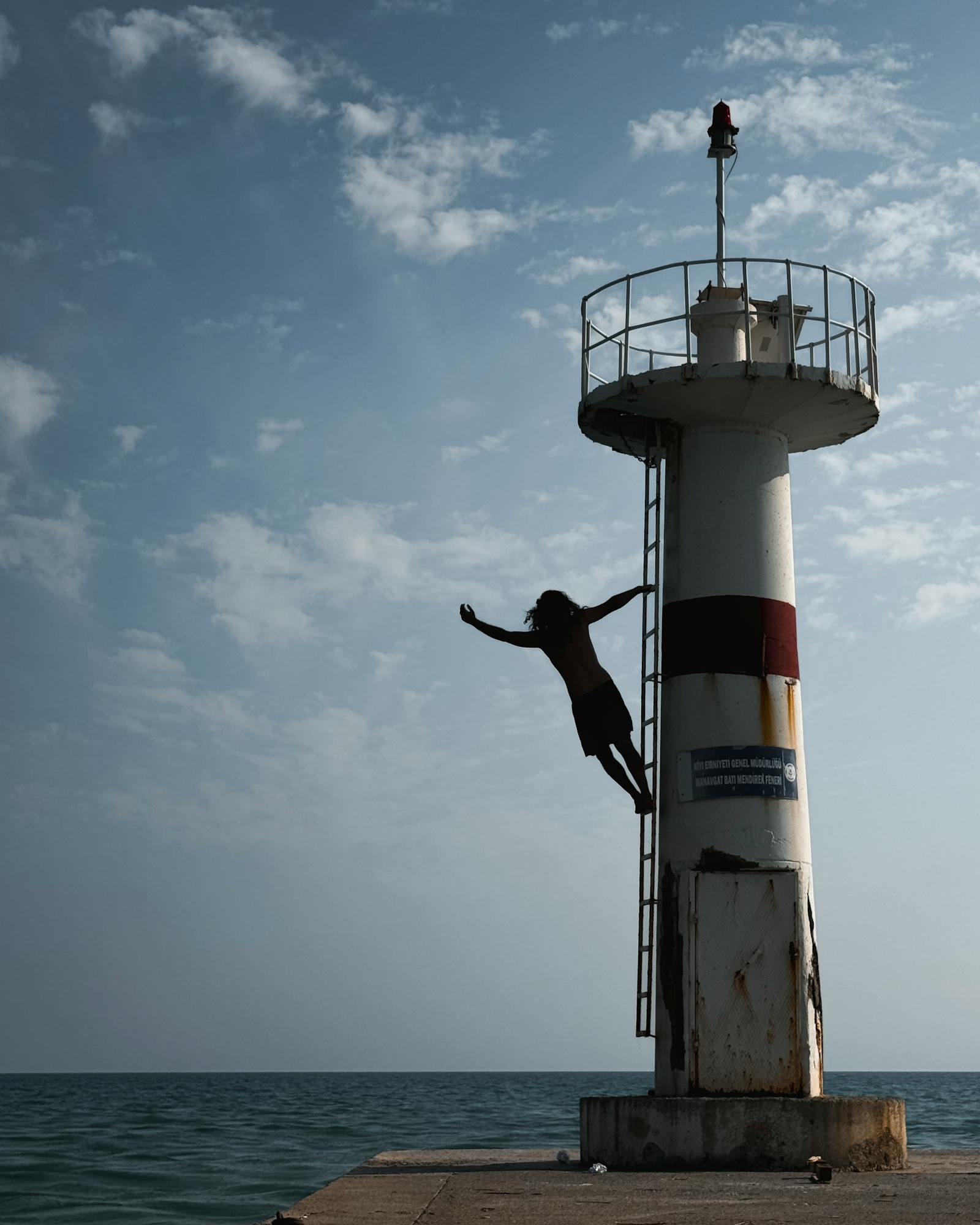 Silhouette of a person jumping from a lighthouse over the ocean under a cloudy sky.