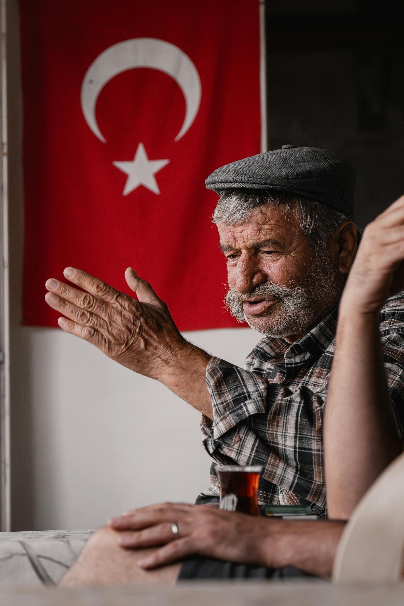 Senior man with mustache having tea in a village setting with Turkish flag. Captured in Seydişehir, Konya, Türkiye.