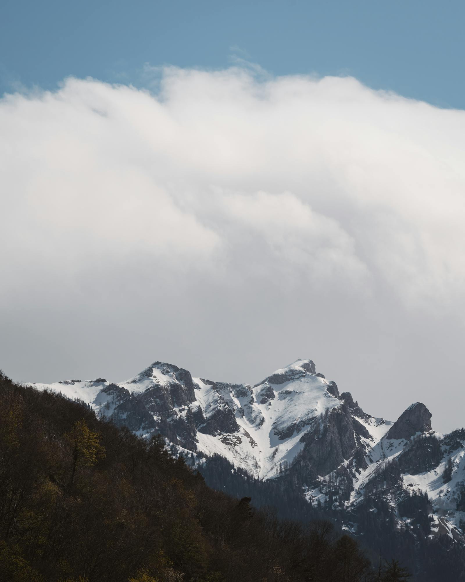 Dramatic snow-covered mountain peaks under a vast cloud-filled sky.