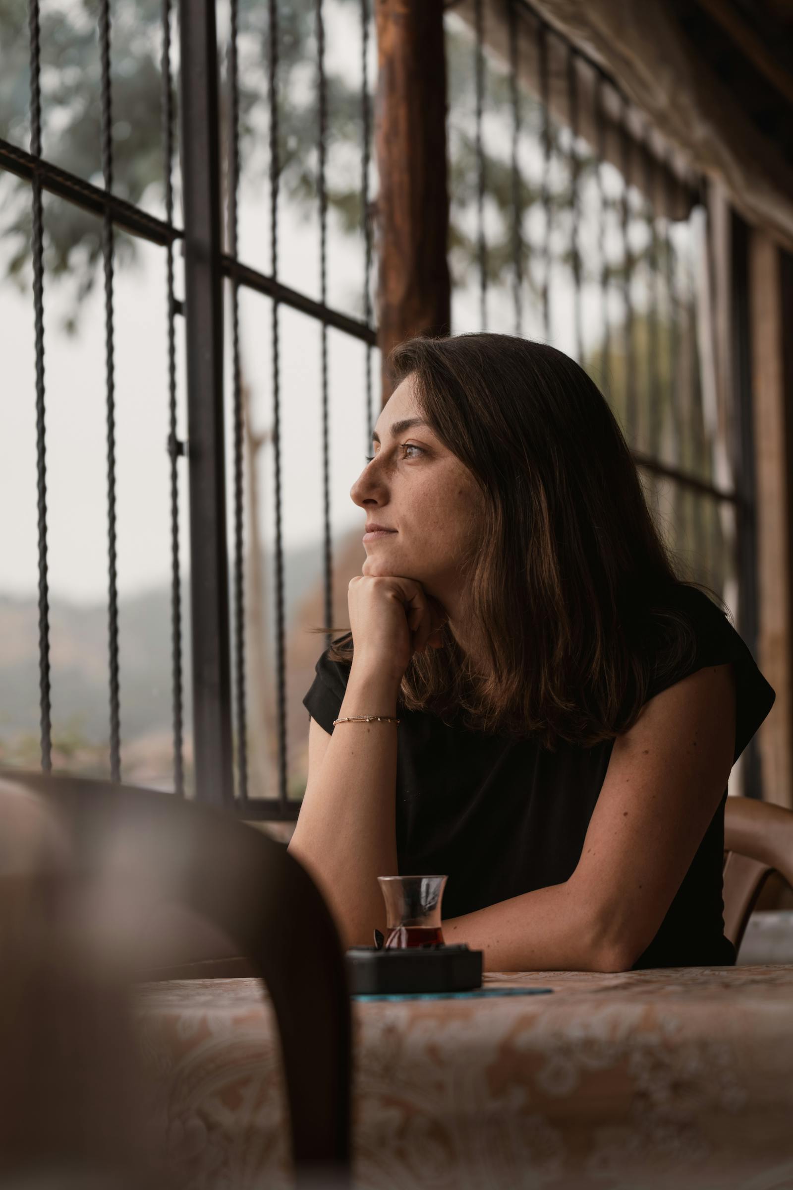 A woman sits in a café, daydreaming as she gazes through the window, reflecting a peaceful moment.