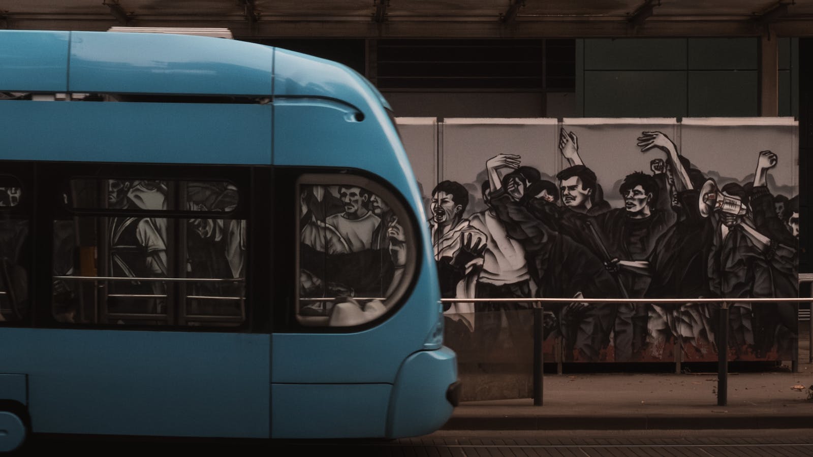 A blue tram moves past a dynamic street art mural depicting expressive urban life in Zagreb, Croatia.