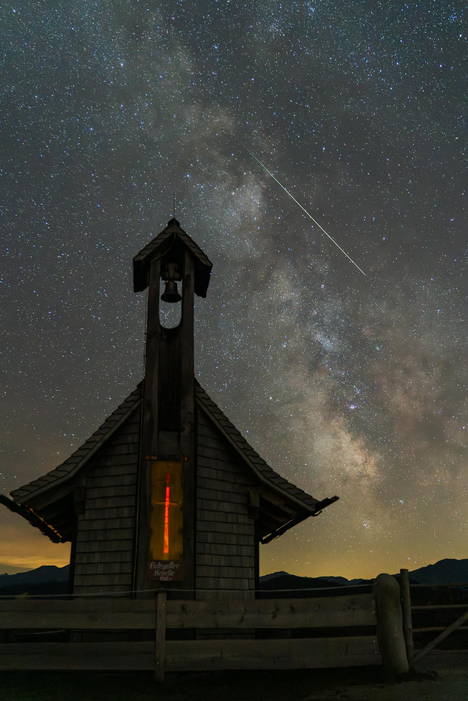 Breathtaking starry night over a chapel in Innsbruck with the Milky Way and meteor shower.