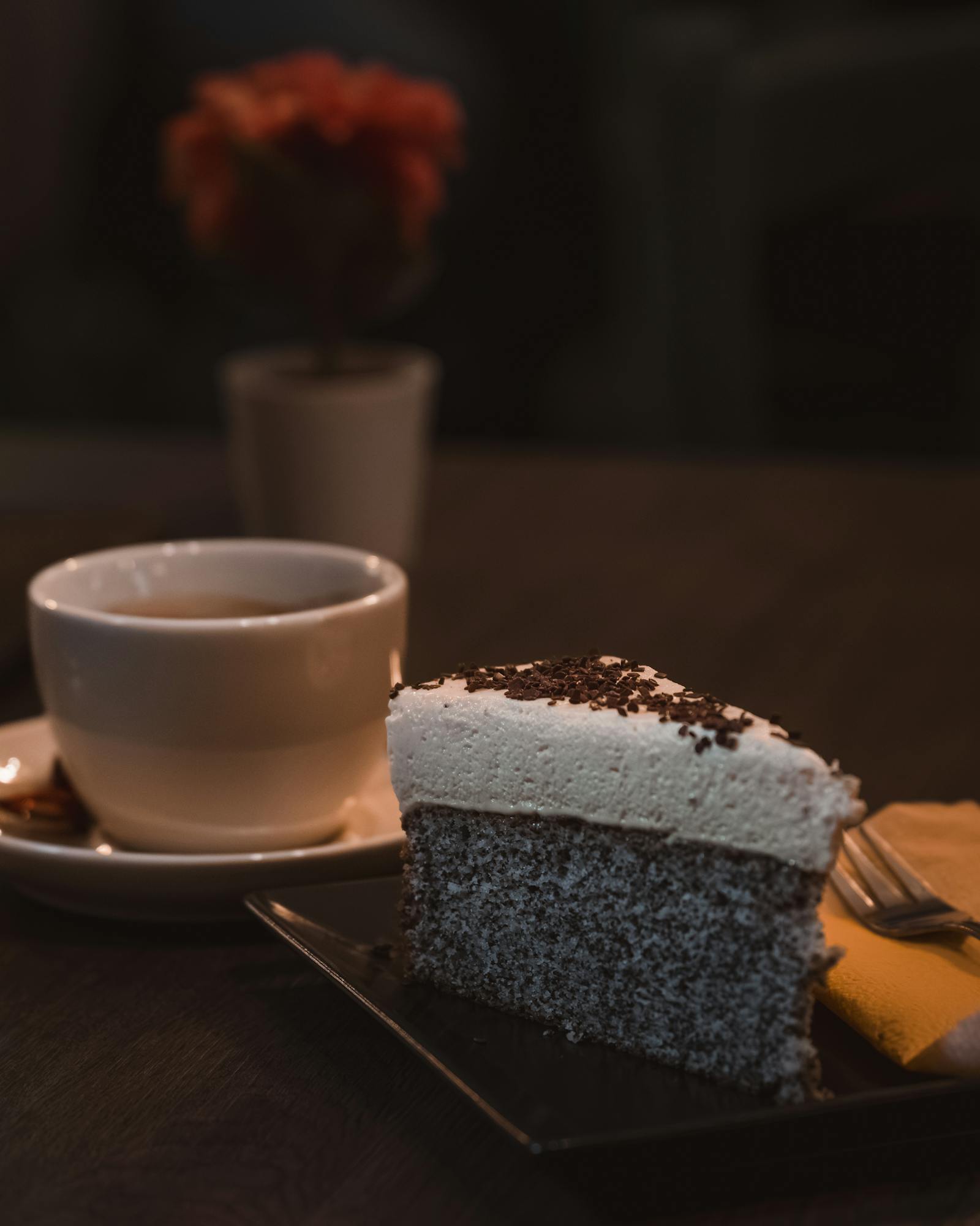 A slice of chocolate cake with a cup of coffee on a wooden table in a cozy cafe setting.