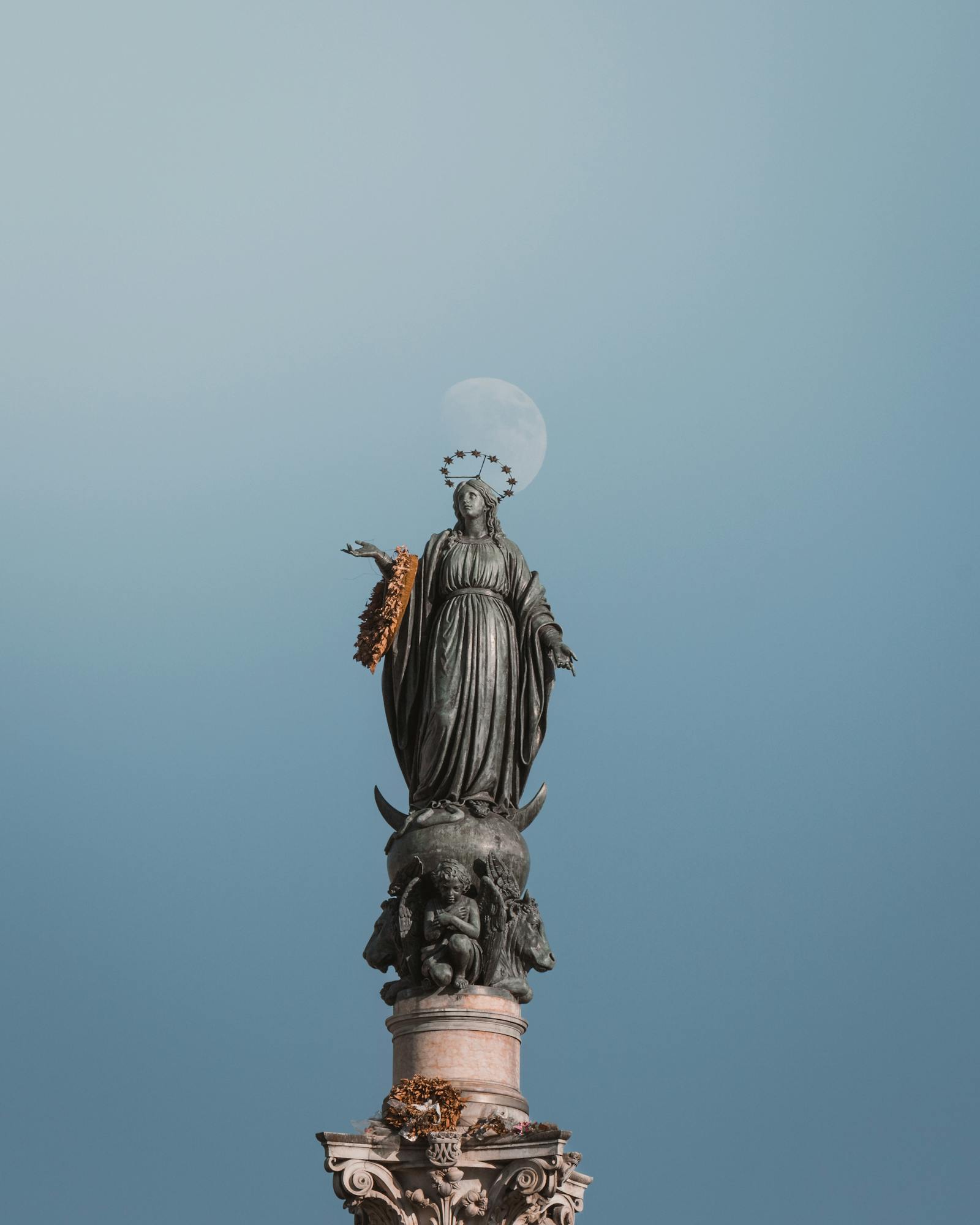 Aerial view of the Immaculate Conception statue in Rome, silhouetted against a clear sky with a visible moon.