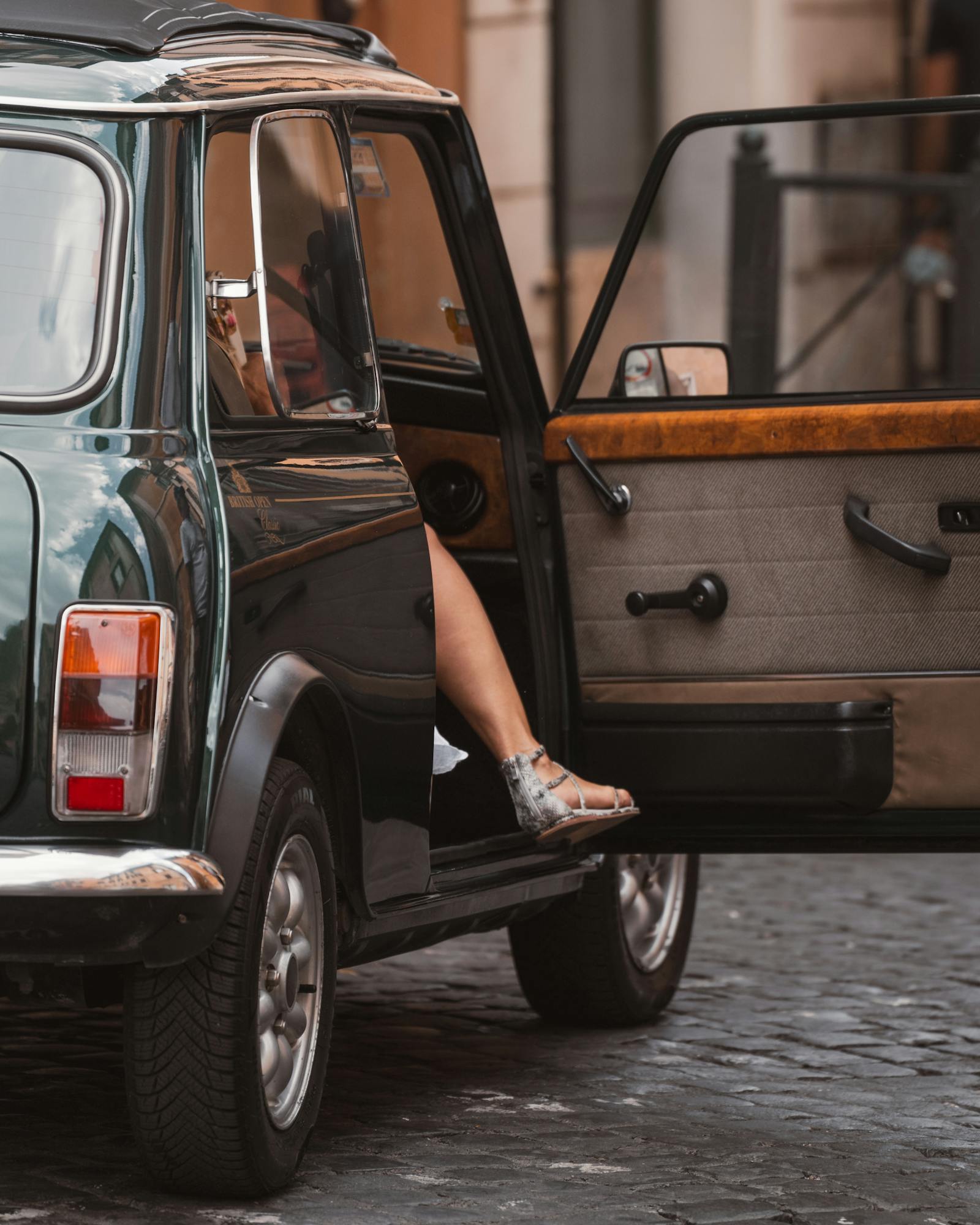 Classic vintage car parked on a cobblestone street in Rome, Italy, with a person's leg visible.