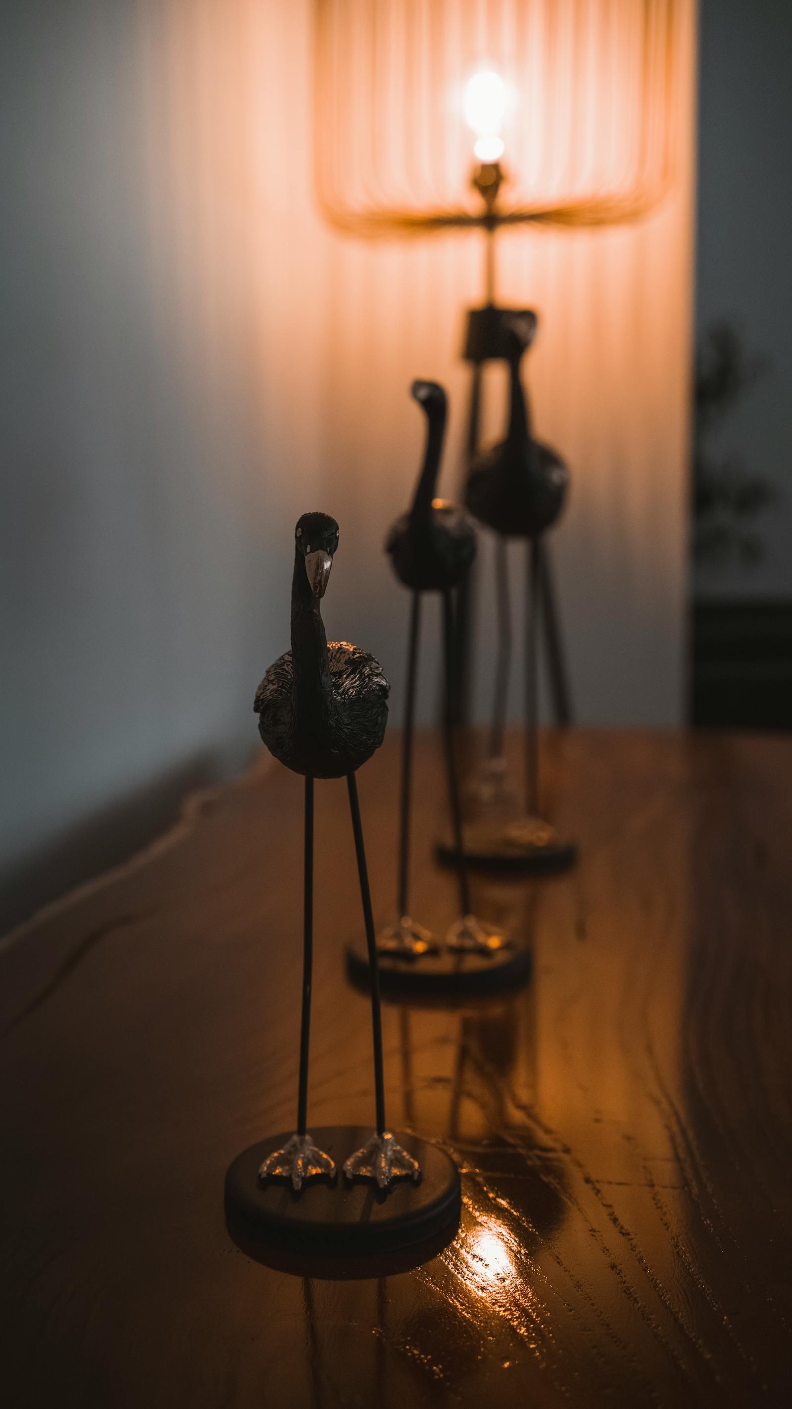 Antique bird sculptures with warm candlelight ambiance on a wooden table, capturing elegance and tranquility.