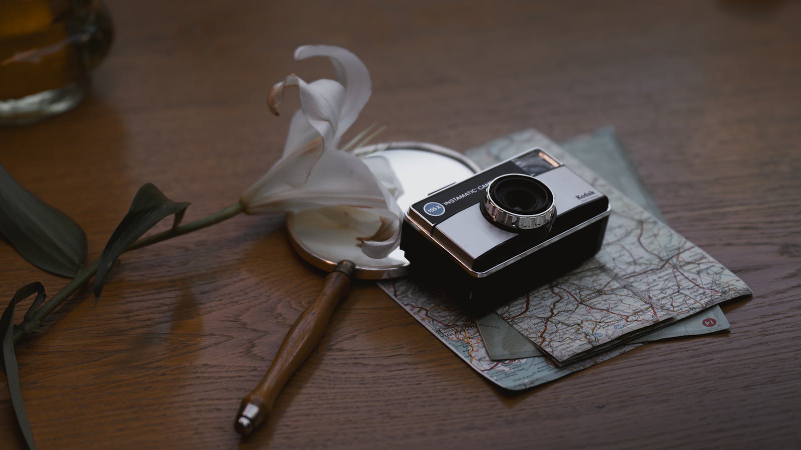 A vintage camera with a travel map and white lily on a rustic wooden table.