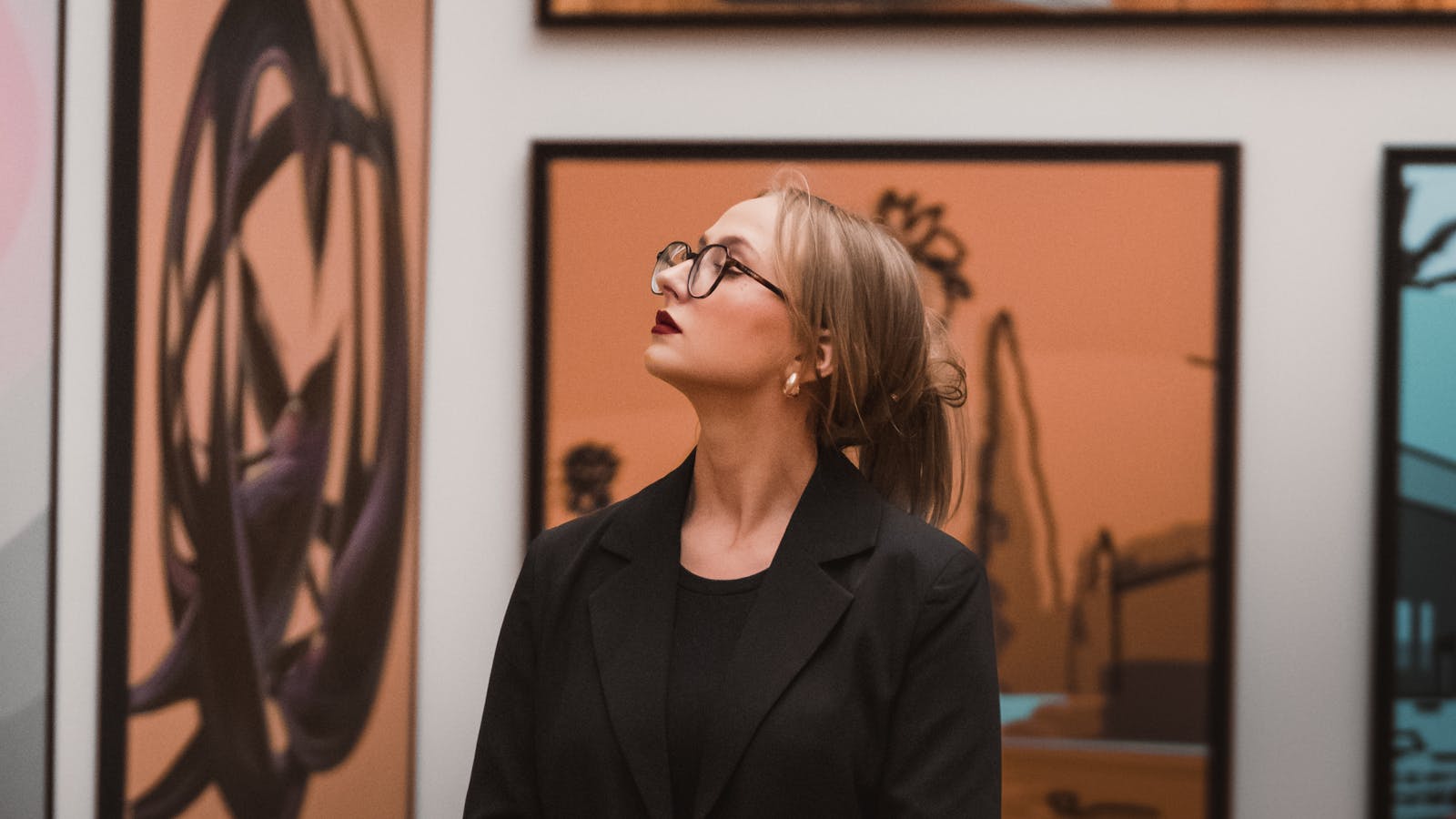 Woman in glasses observing modern art in a gallery setting, deep in contemplation.