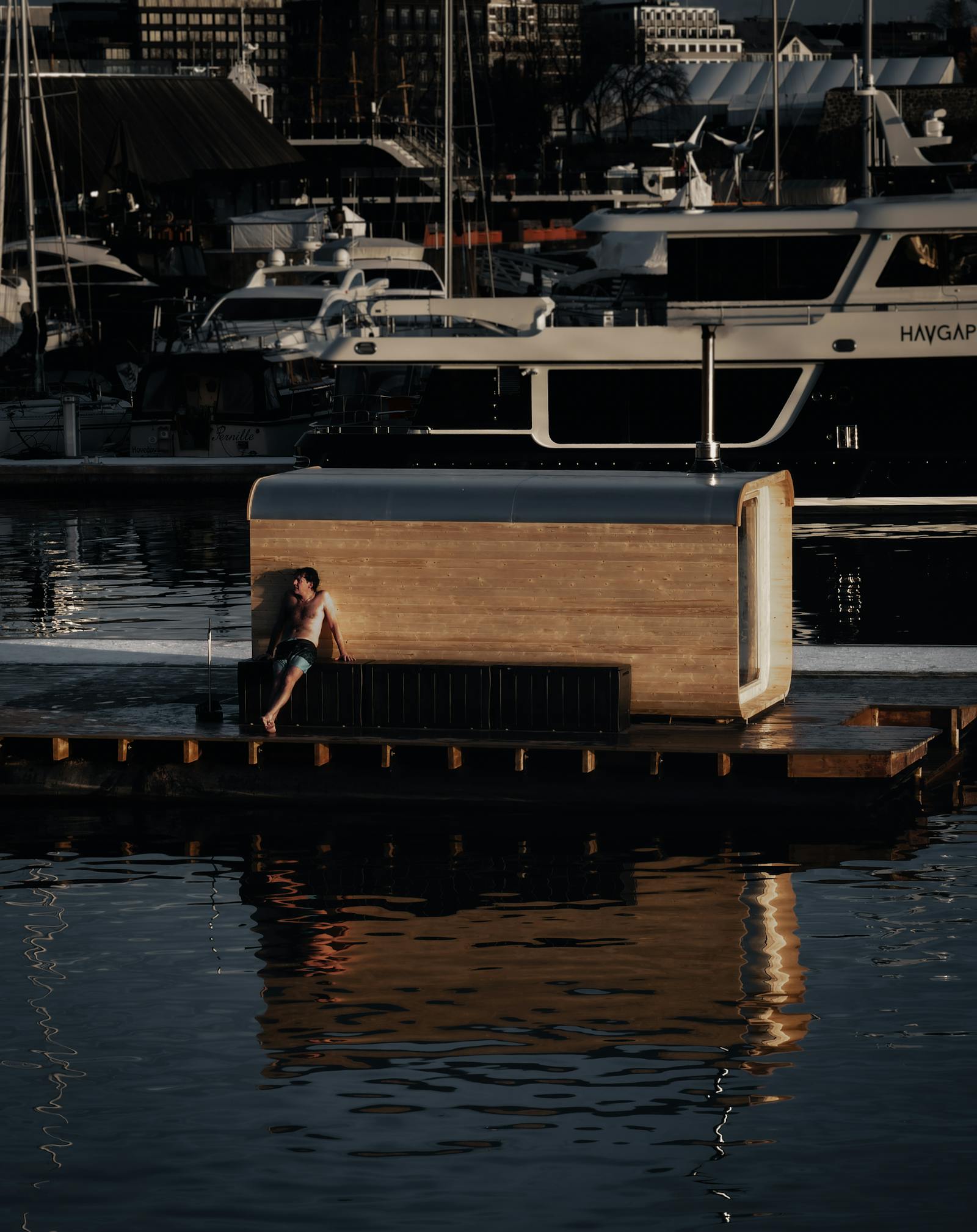 A person relaxes on a dockside floating house in Oslo marina during a tranquil sunset.