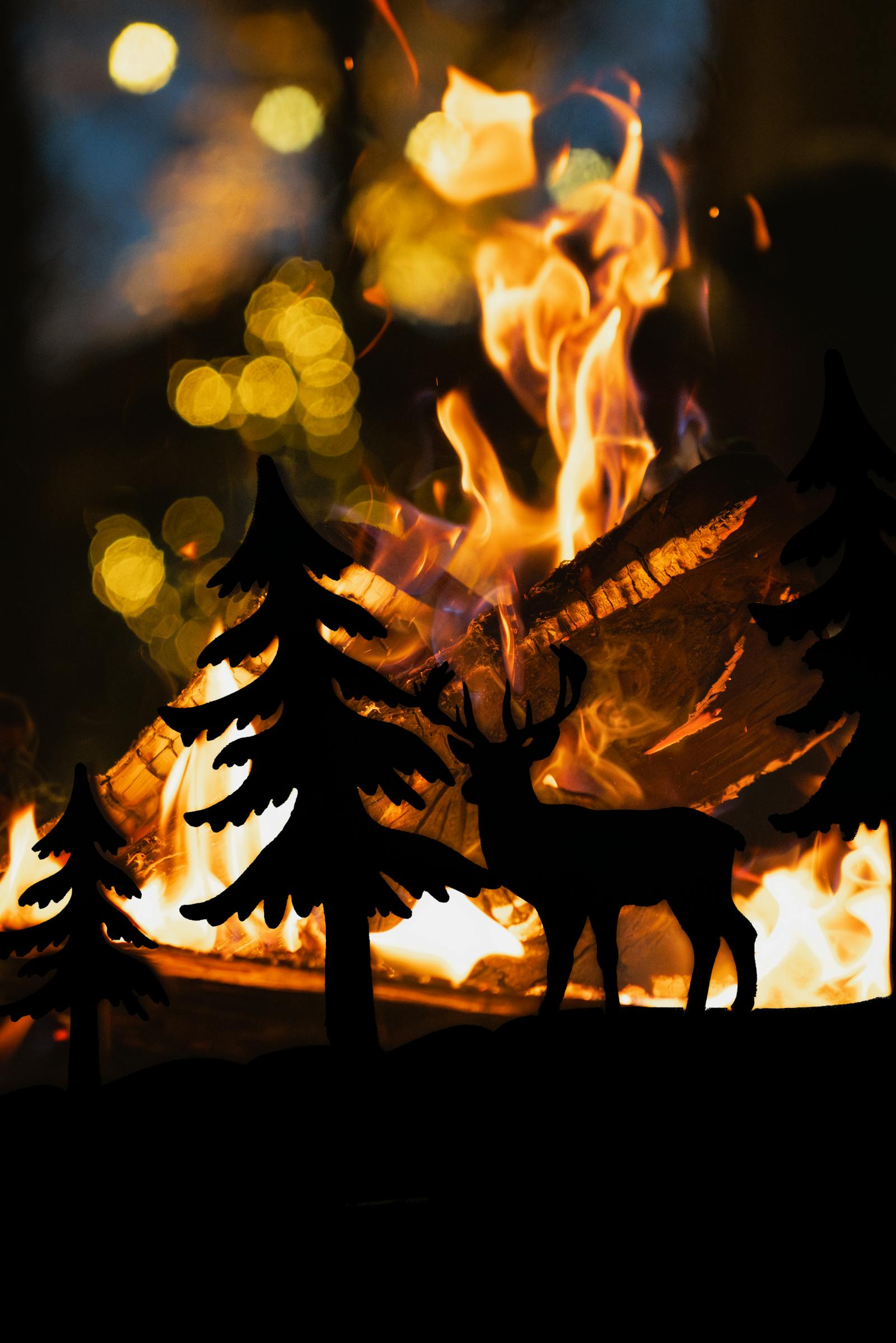 Silhouetted deer and pine trees create a serene scene against a warm bonfire glow. Perfect for holiday ambiance.