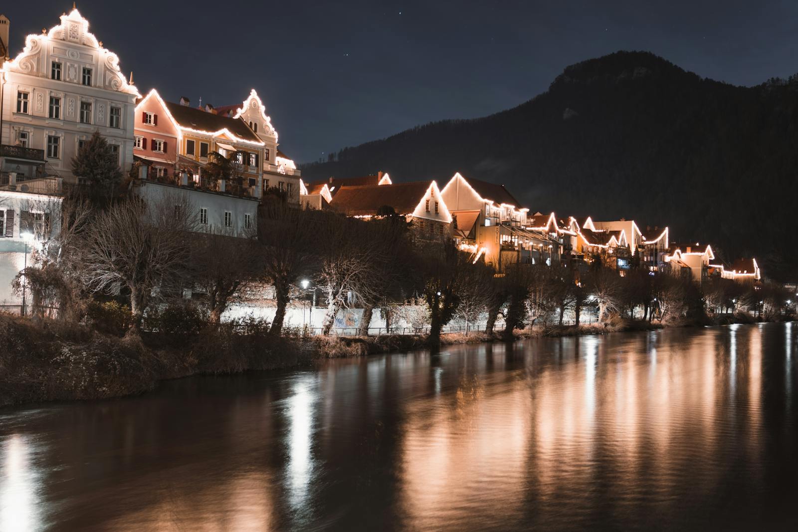 Illuminated houses along the river in Frohnleiten, Austria, creating a serene night scene.