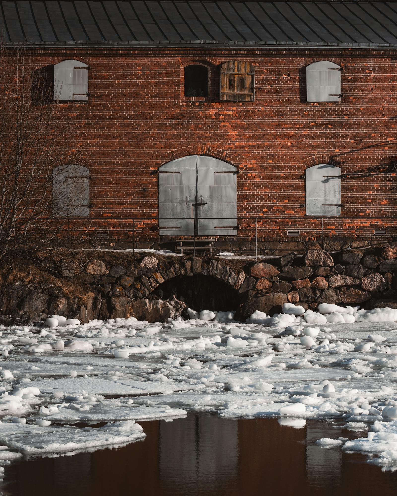 Old brick building by a frozen river in Helsinki. Winter scene with ice formations.