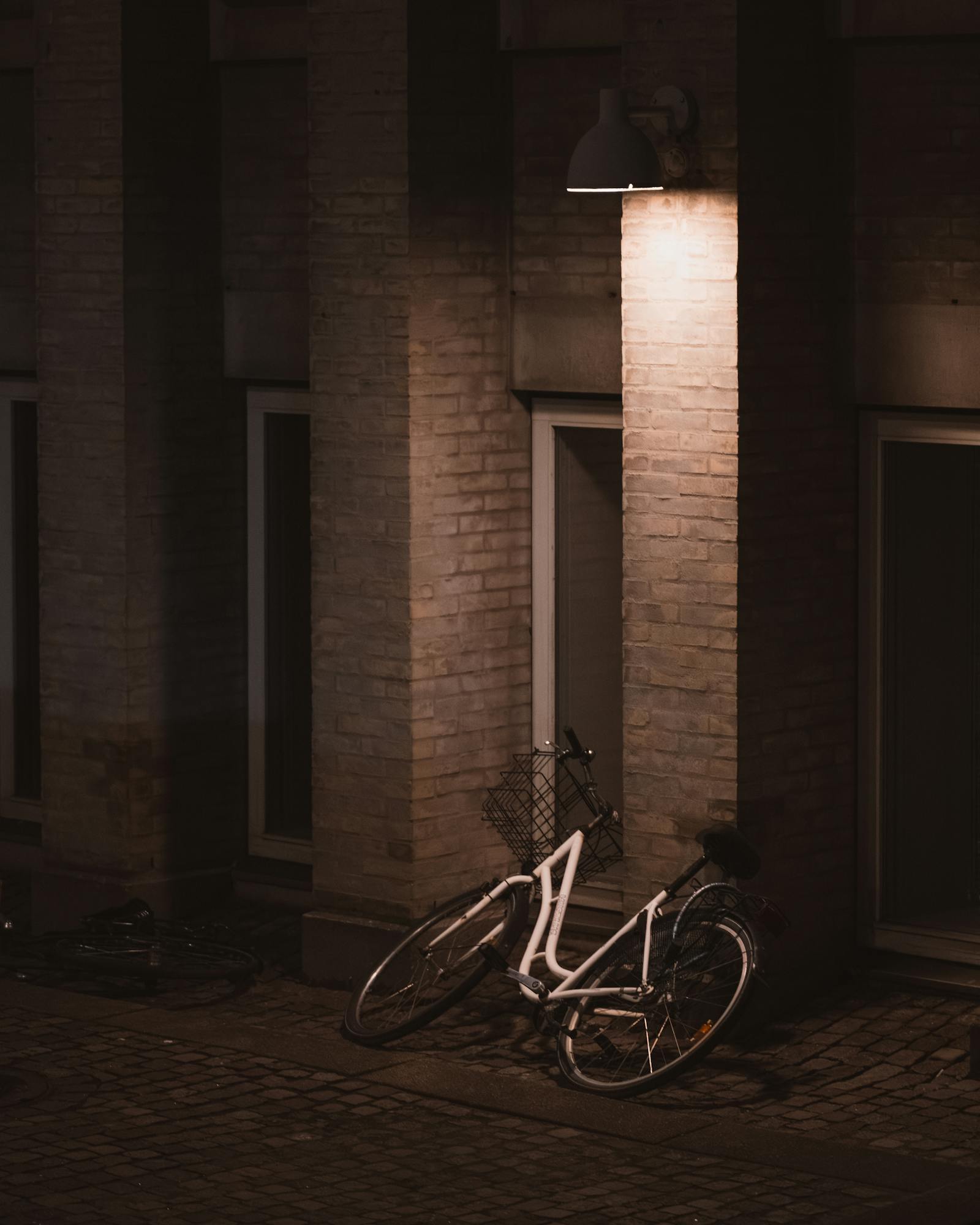 Nighttime urban scene with a bicycle against a brick wall under streetlamp.